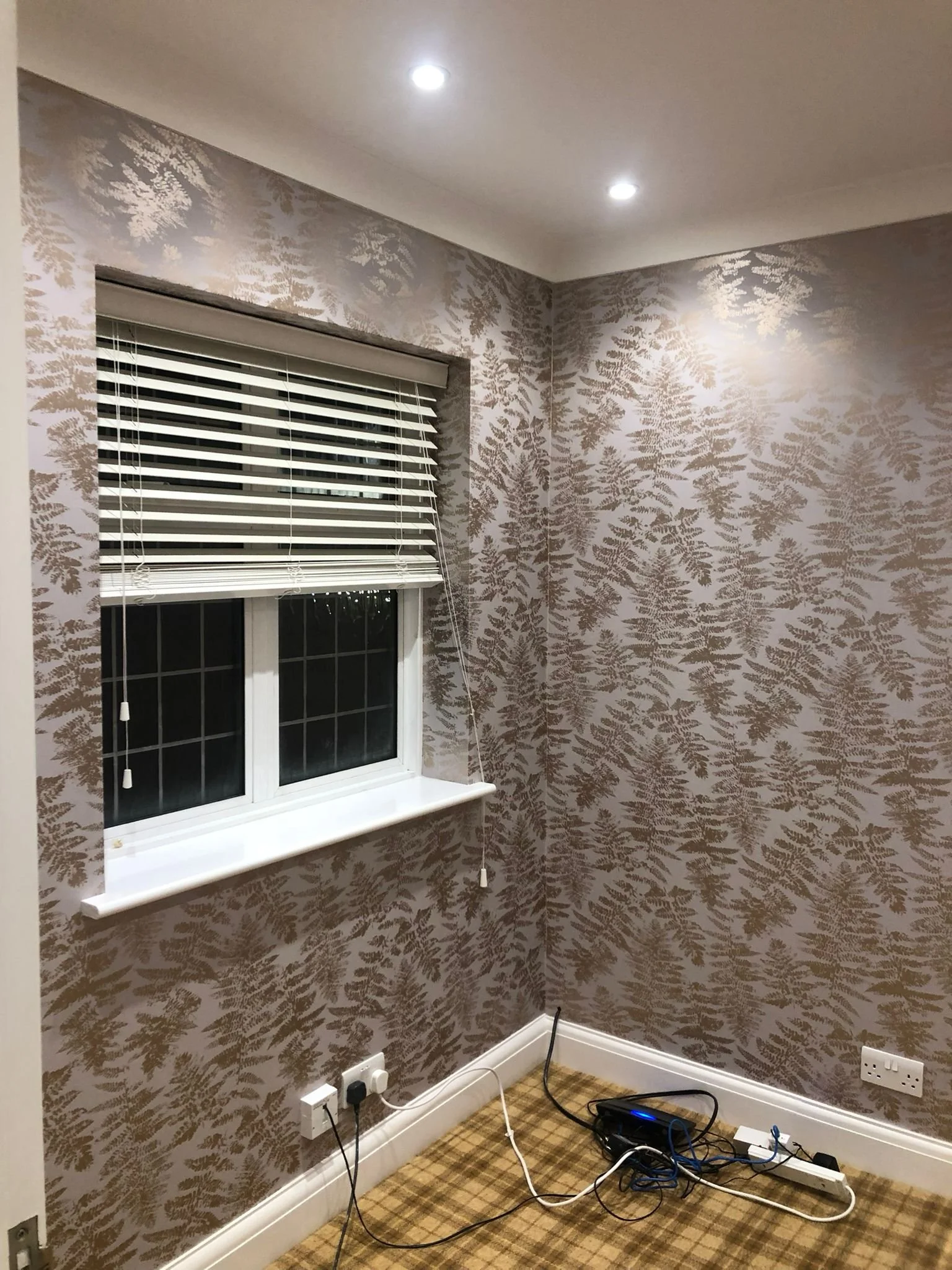 Empty room with patterned wallpaper, a window with blinds, and tangled electrical cords on the floor.