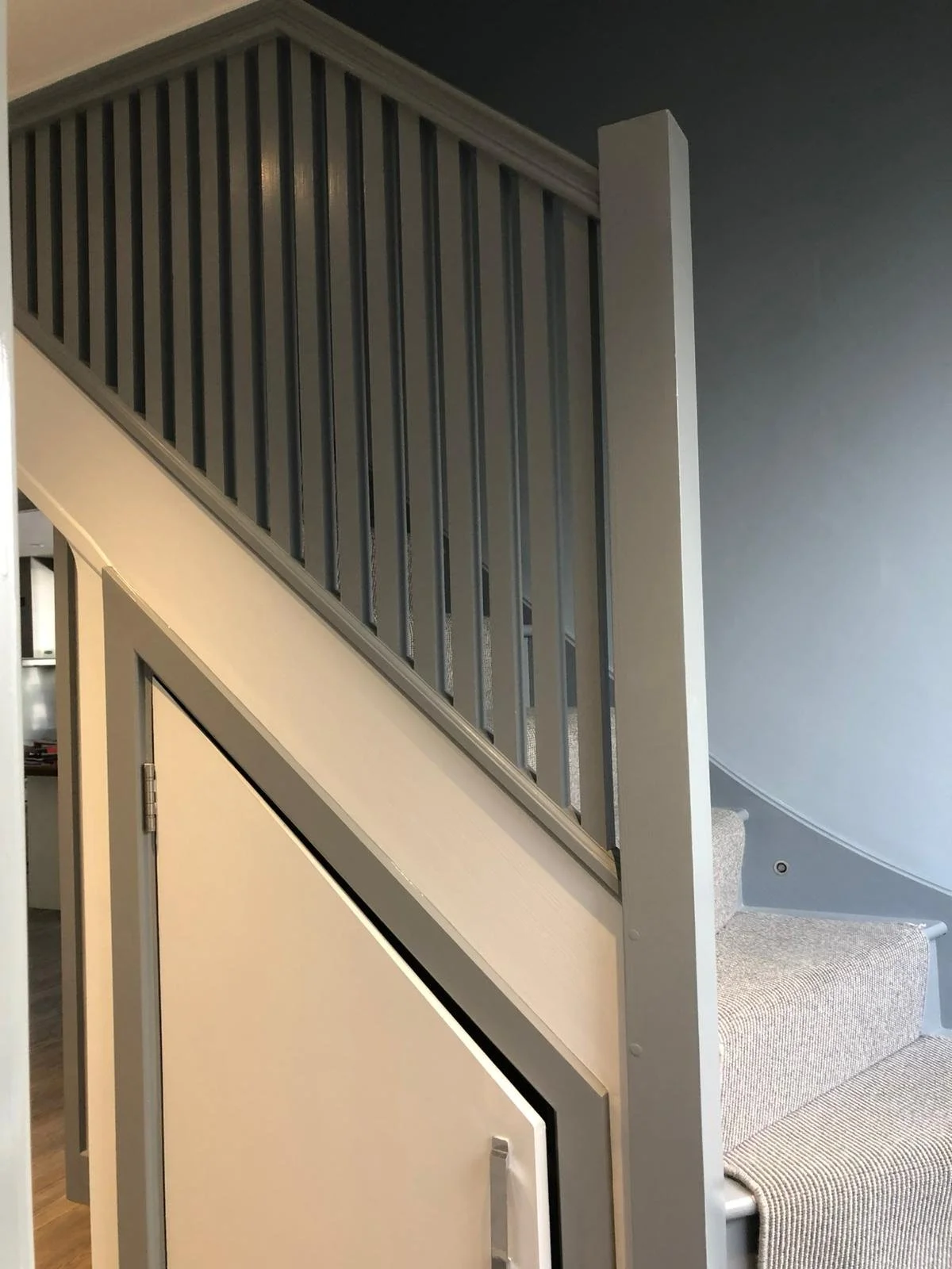 Indoor staircase with beige carpeted steps and a wooden bannister with gray vertical slats.