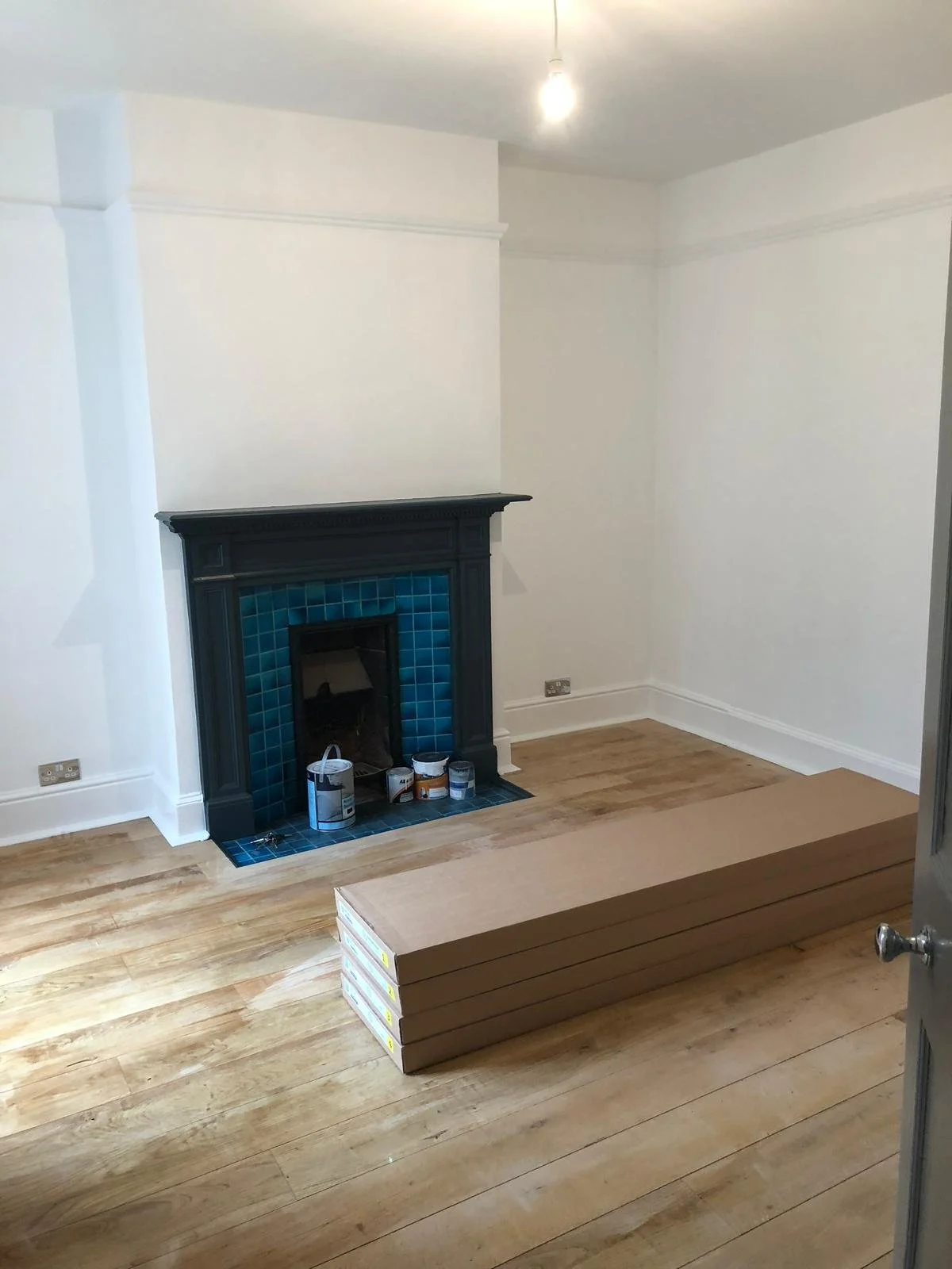 Empty room with a black fireplace surrounded by blue tiles, hardwood floor, and a stack of three cardboard boxes in the foreground.