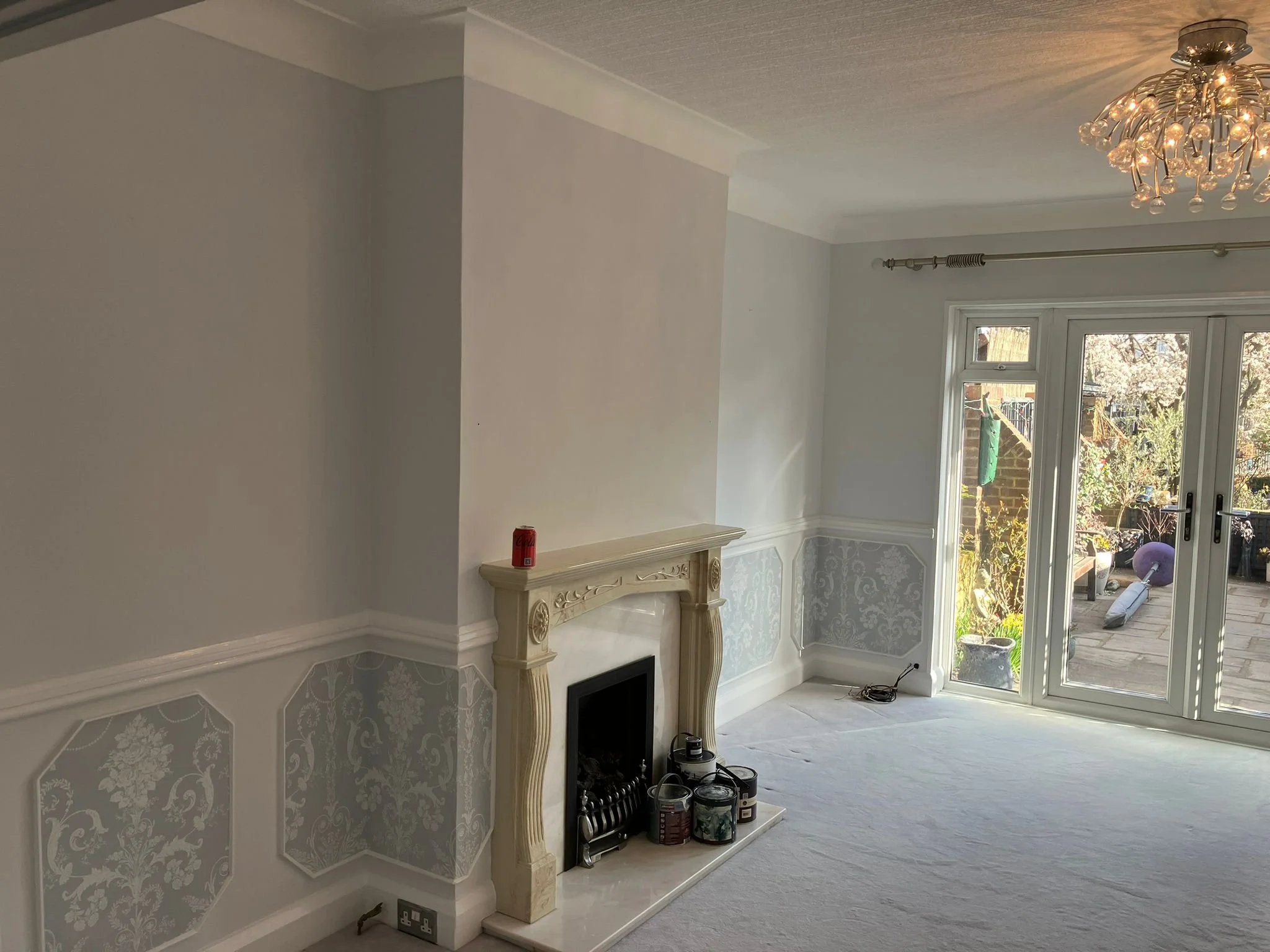 Living room with a fireplace, chandelier, and French doors leading to a garden.
