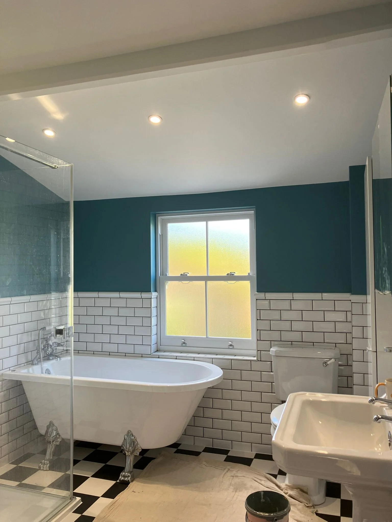 A bathroom with a clawfoot bathtub, a sink, a toilet, and a window, with tile walls and black-and-white checkered floor.