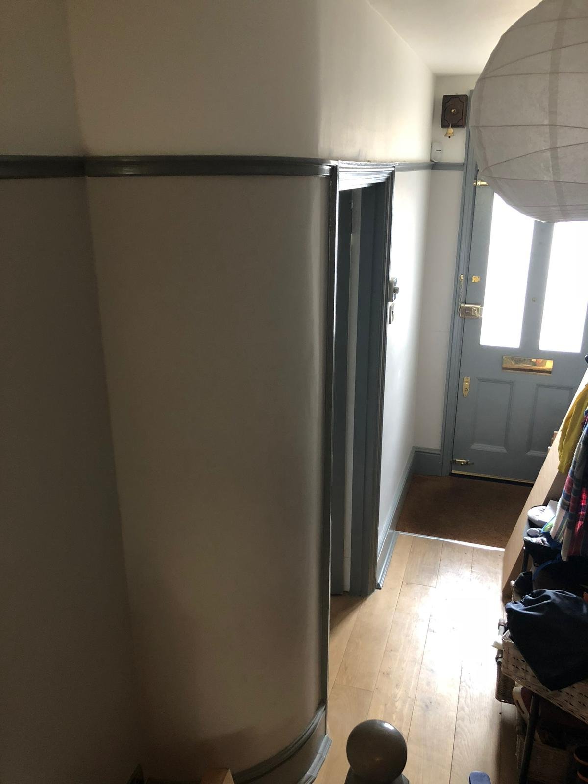 View of an entryway with a gray front door, wooden floor, small bench with clothing, and a large umbrella in the corner.