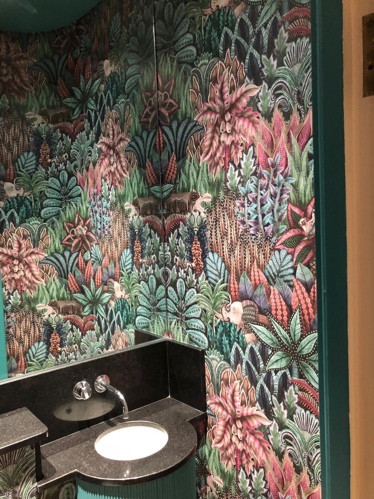 Brightly colored jungle-themed wallpaper with various tropical plants, animals, and insects surrounding a small black granite sink.