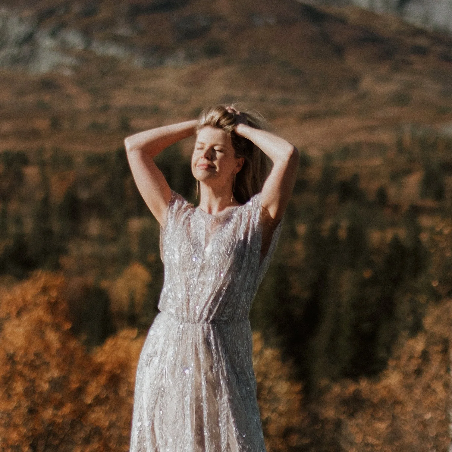 Olga running her fingers through her hair as the sunlight illuminates her, surrounded by autumn trees and mountains.
