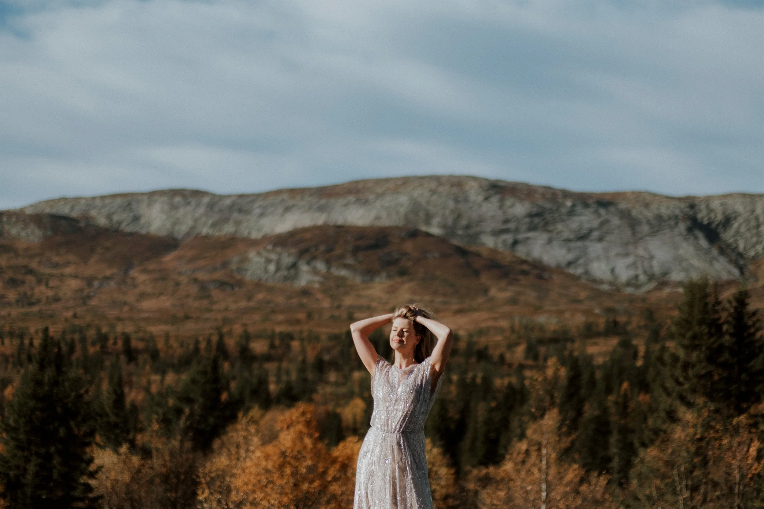 Olga running her fingers through her hair as the sunlight illuminates her, surrounded by autumn trees and mountains.