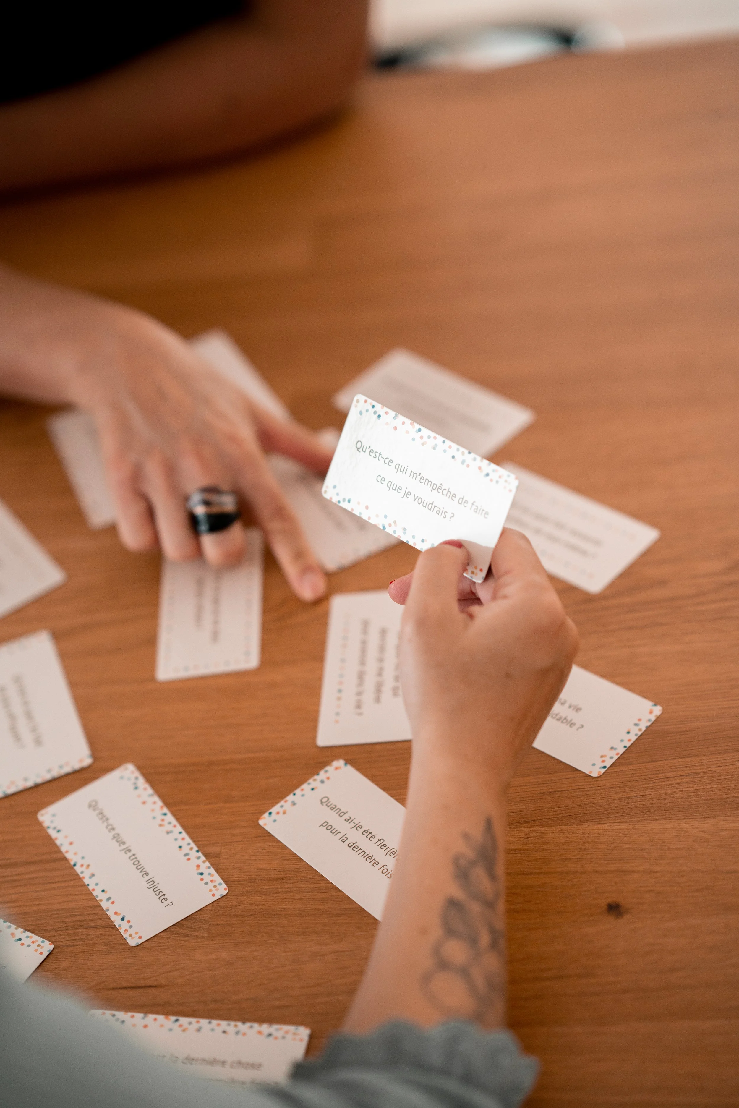 Deux mains tenant des cartes de jeu, avec plusieurs autres cartes sur une surface en bois.