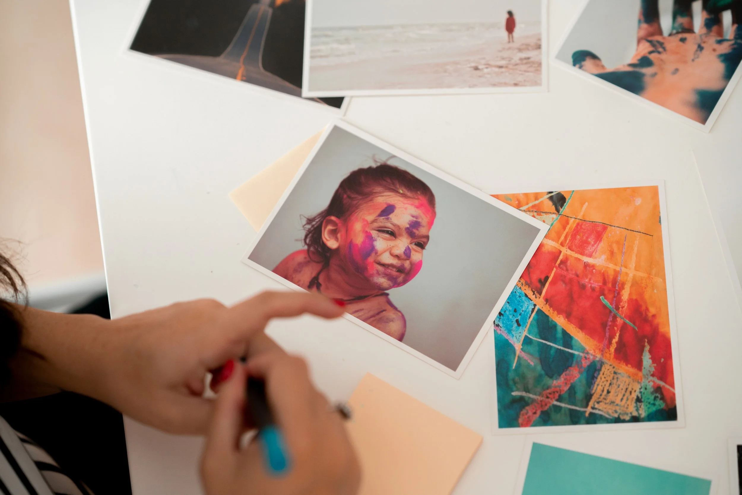 Une personne écrit ou dessine à côté de plusieurs photos et œuvres d'art colorées sur une table.