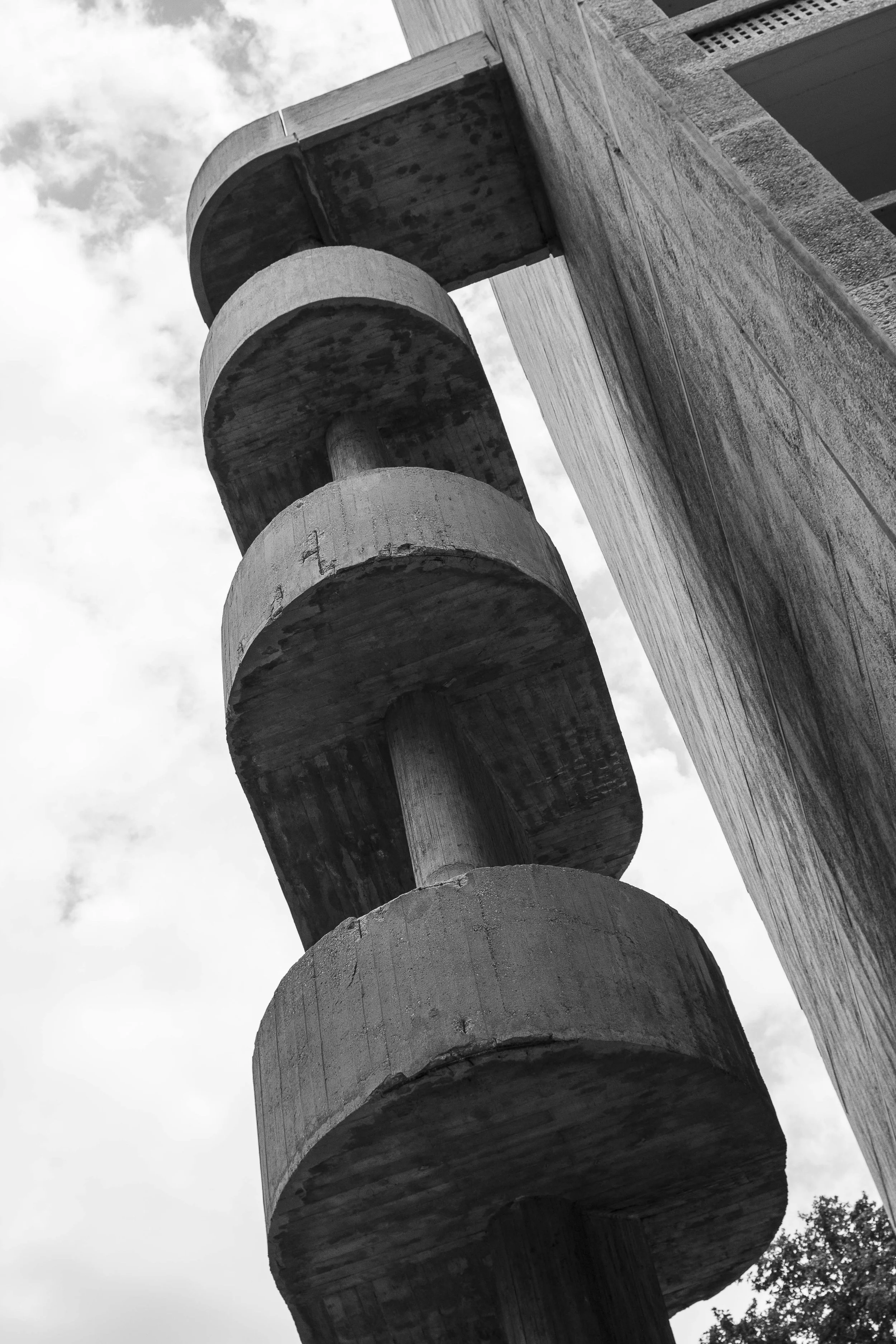 Black and white photo of a Brutalist stairwell, showing the rounded edges of each level and part of a brick wall structure on the right.