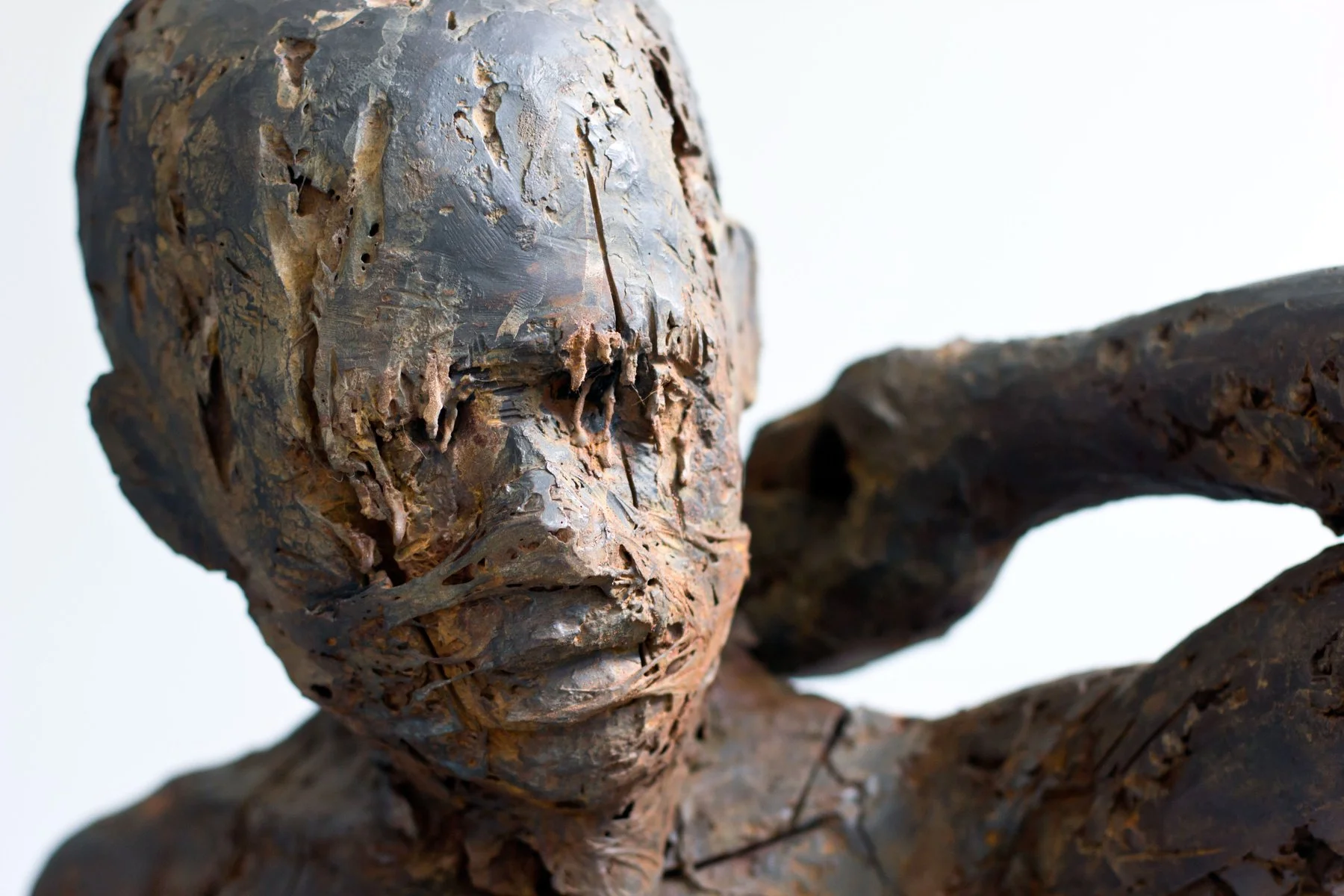 Close-up of a rusted metal sculpture of a child's face and hand, with a white background.