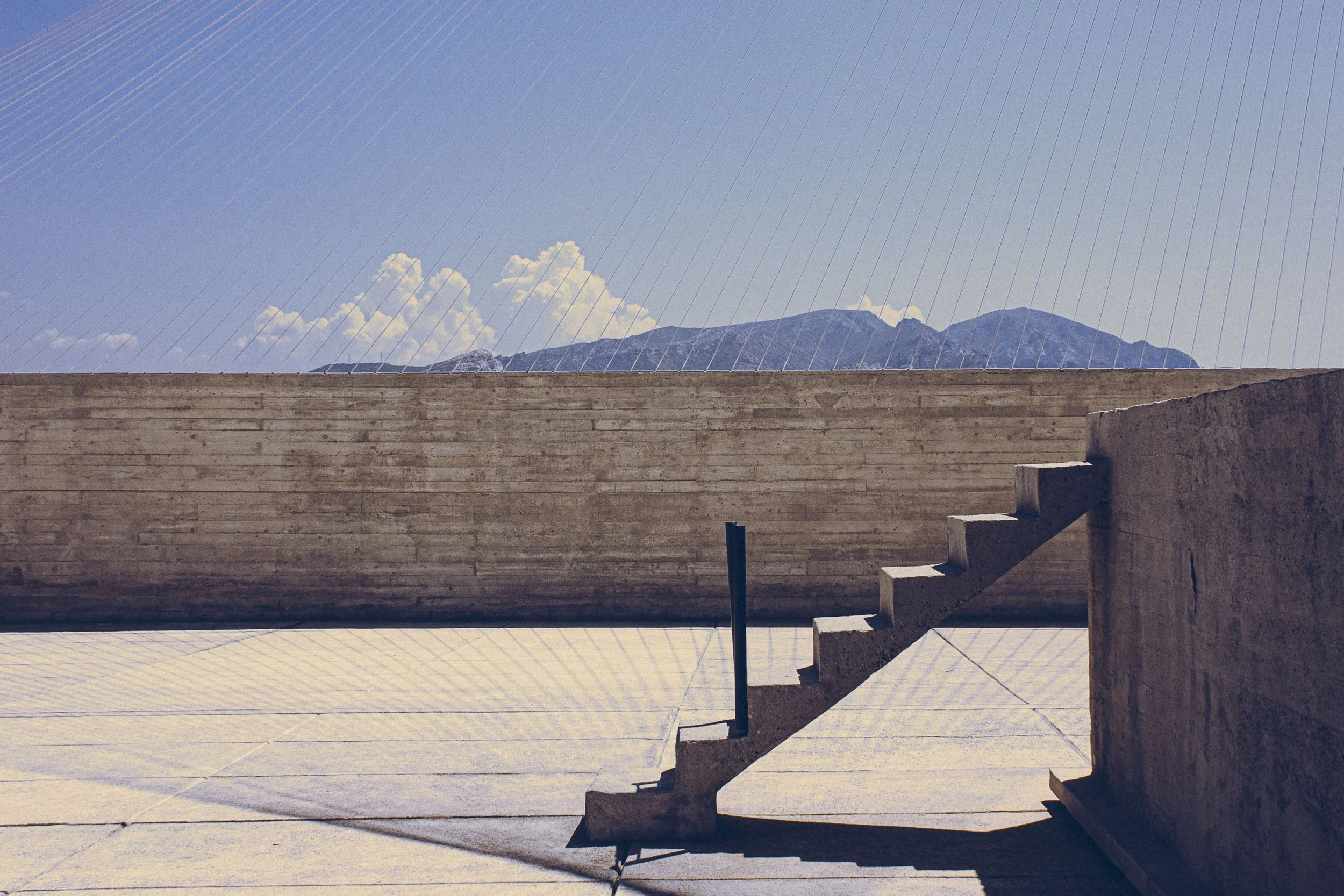 Minimalist outdoor scene featuring a concrete staircase and wall with a view of mountains and sky in the background.