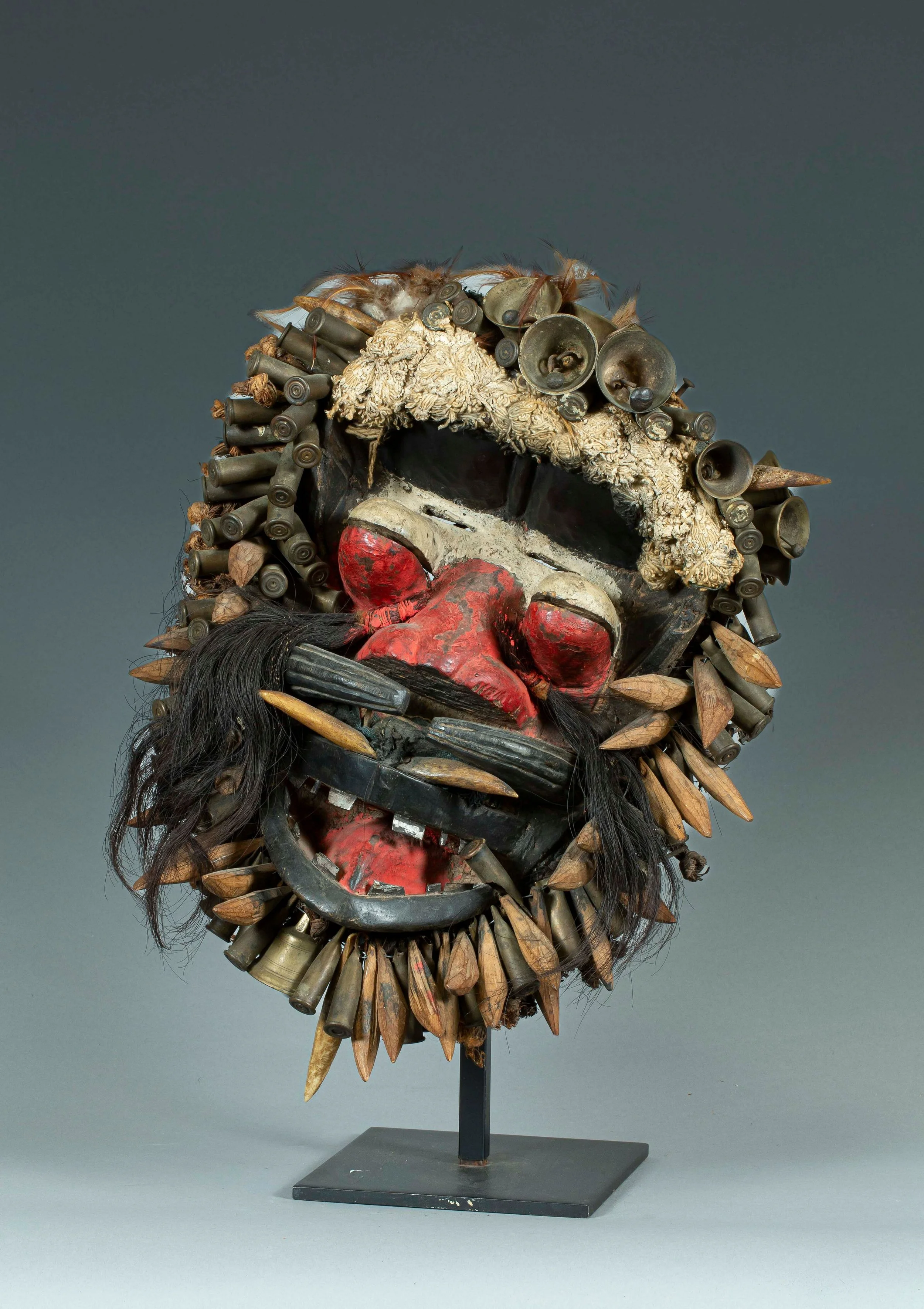 An art mask made of various found objects including bullets, shells, fake hair, and painted facial features.