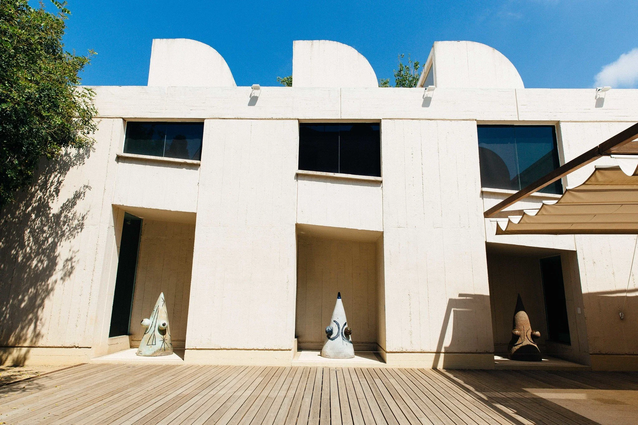 Modern white building with large windows and artistic sculptures on a wooden deck