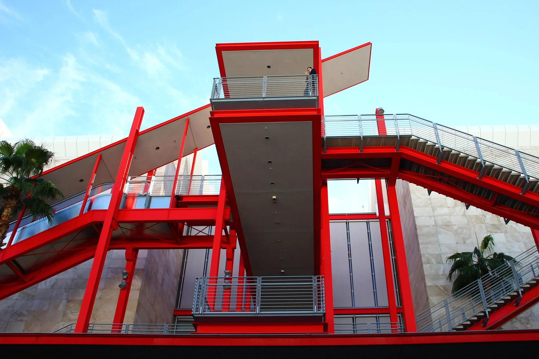 Red modern outdoor staircase and walkways against a blue sky, with a person standing on the upper level.