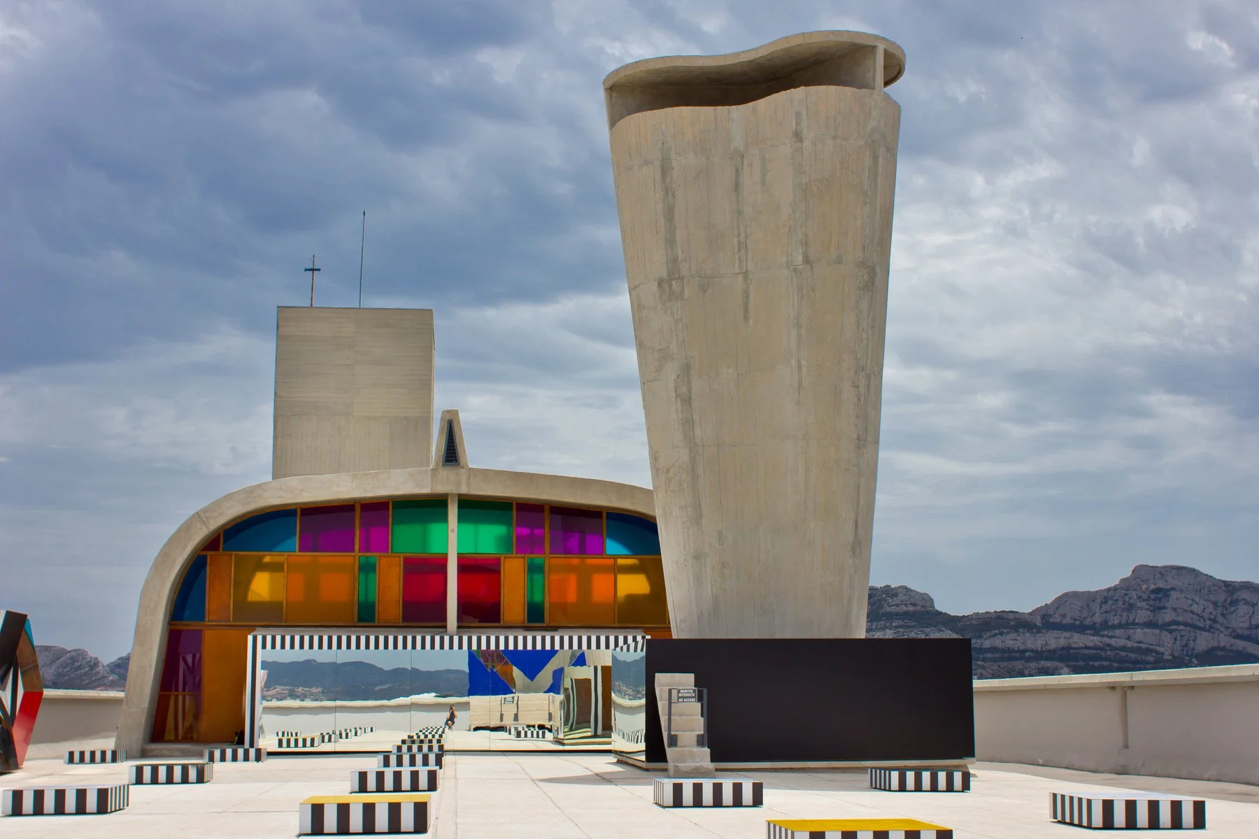 Modern architectural building with colorful stained glass windows and large concrete sculpture, set against a mountain backdrop.
