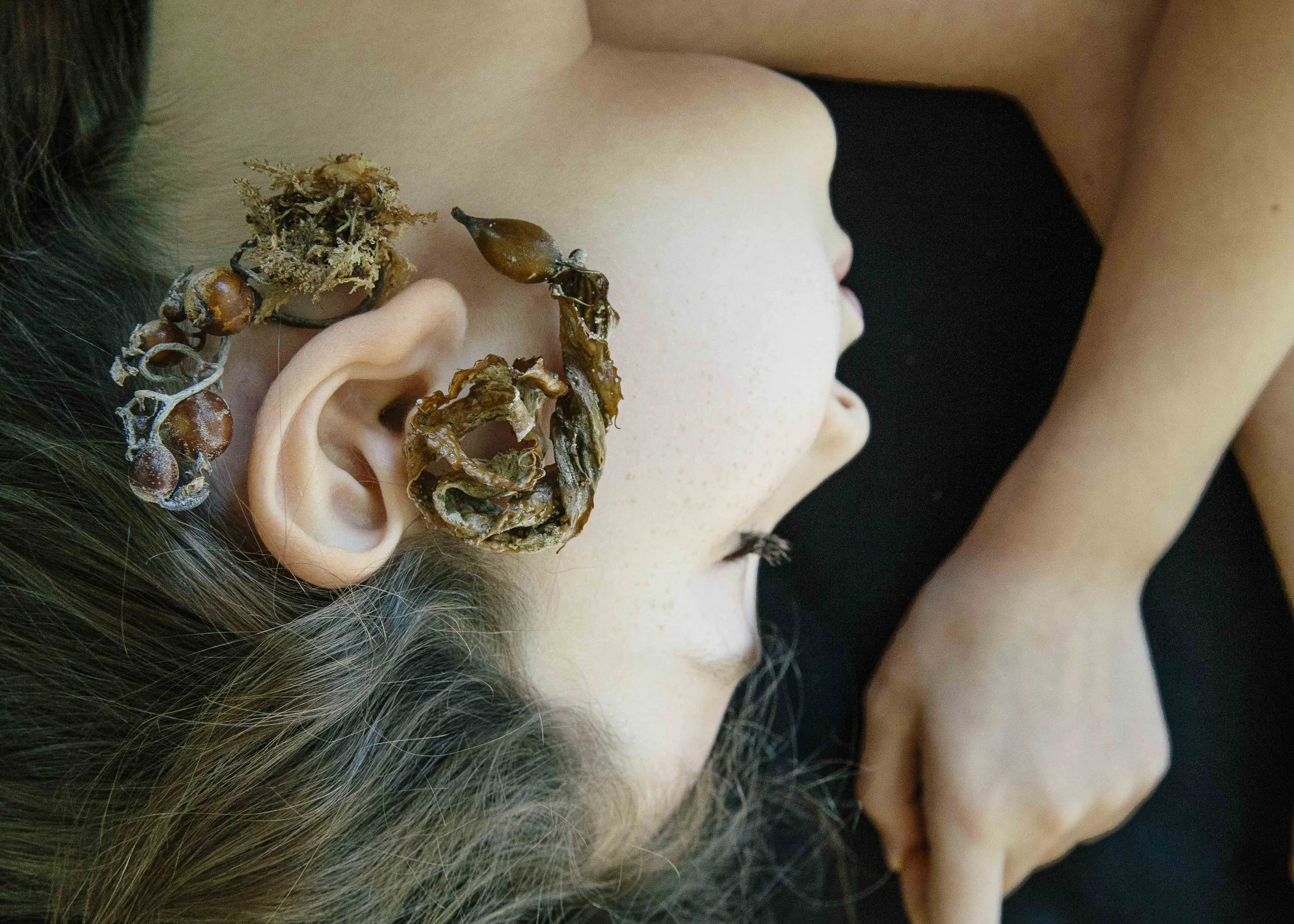 Close-up of a person's ear lying down with dried seaweed on a black background.