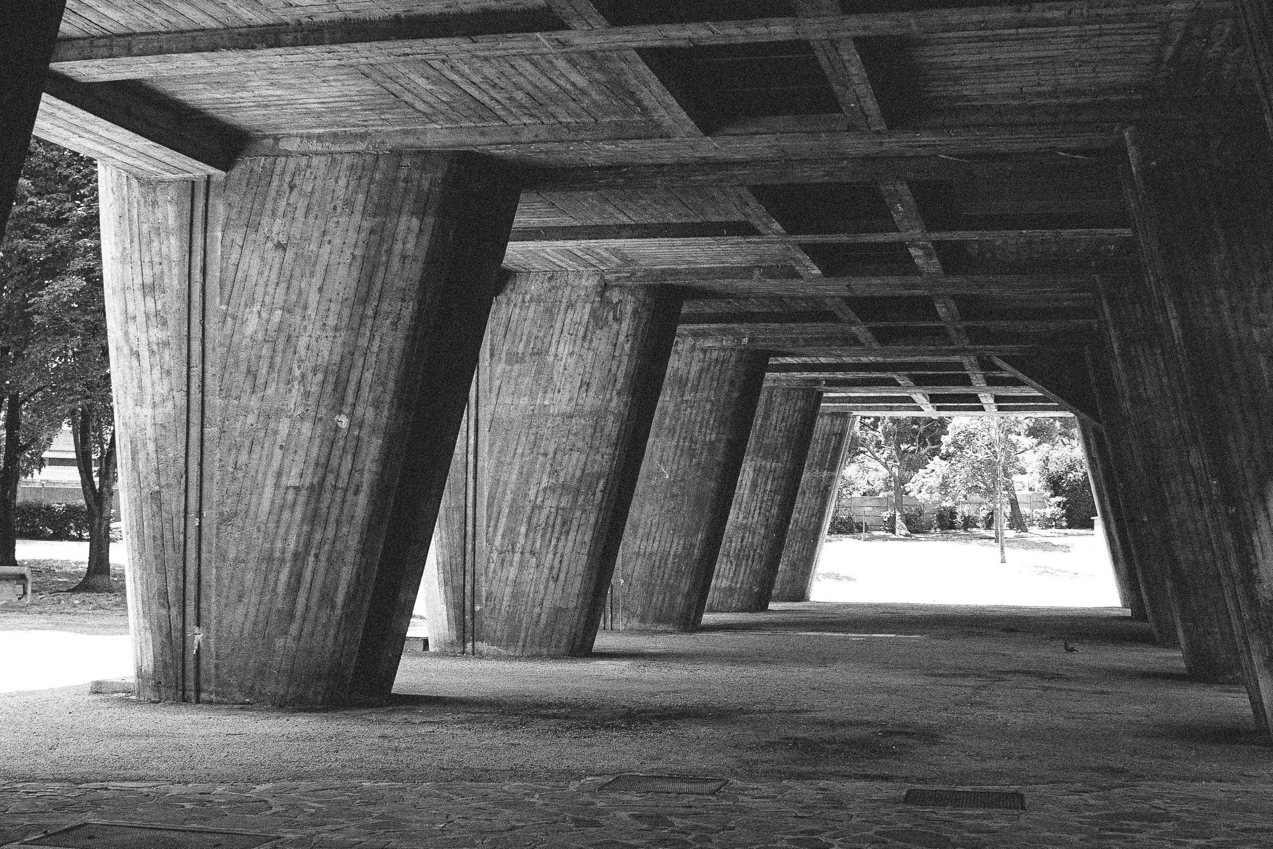 Underground passageway with concrete walls and ceiling, leading to a park with trees and grass visible in the background.
