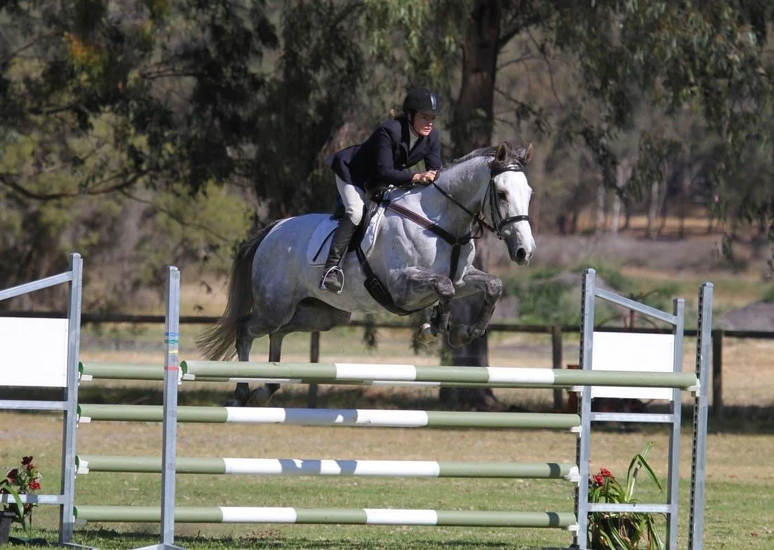 A person riding a gray horse jumping over an obstacle during equestrian show jumping competition.