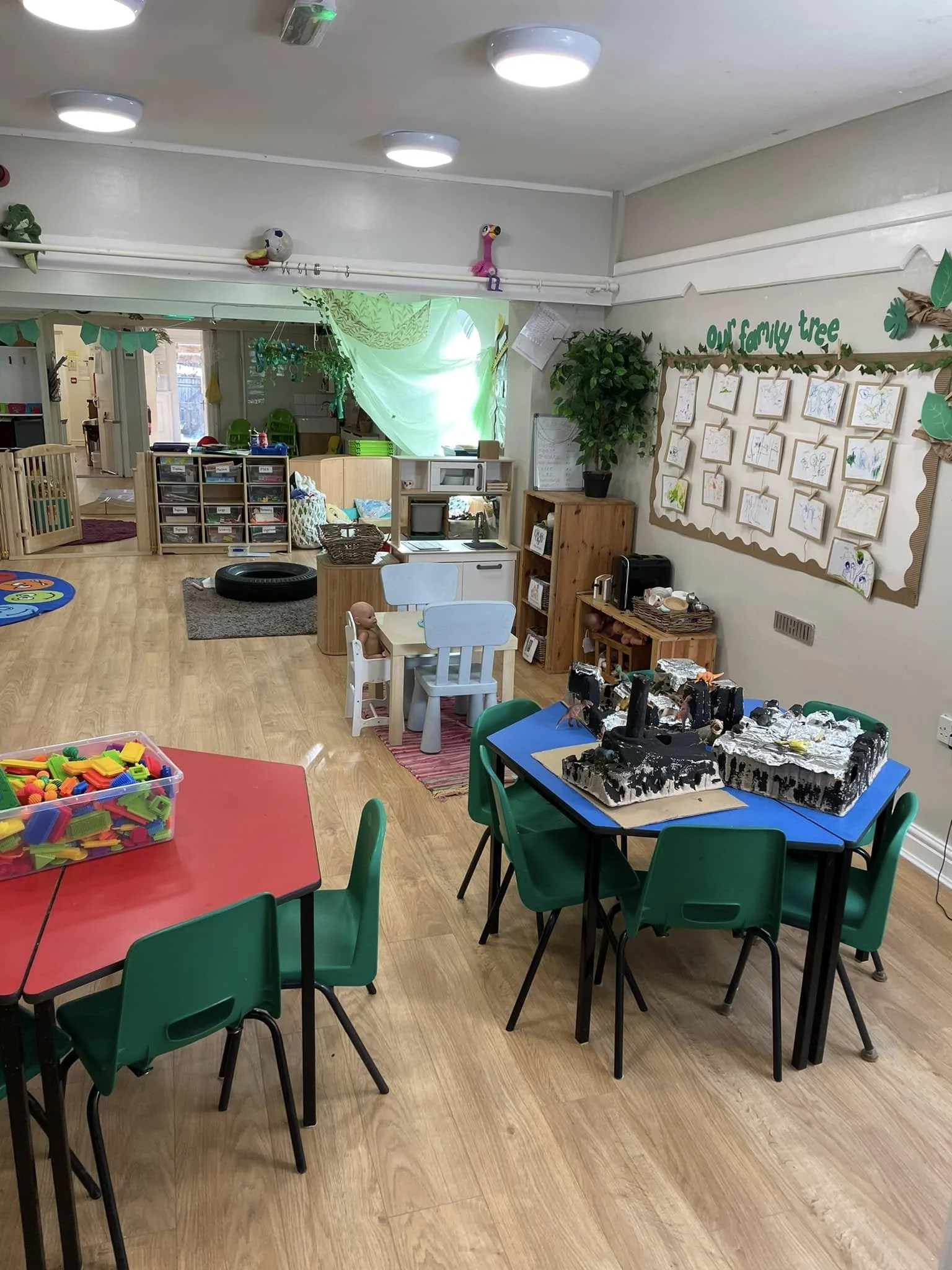 An indoor preschool classroom with colorful tables and chairs, wall art, toys, and children's artwork on display.