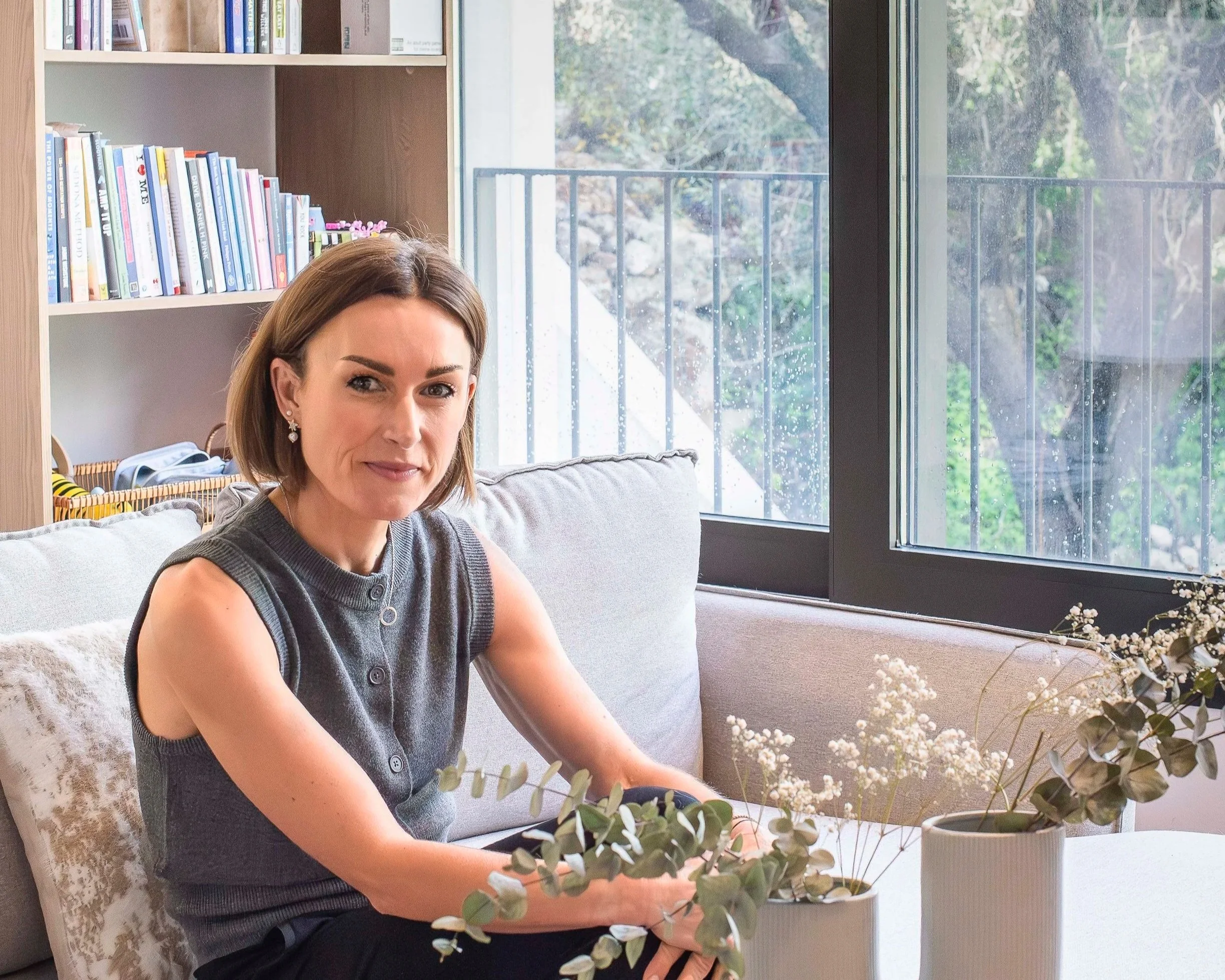 Portarit photo of a woman Laura O'Shaughnessy in a grey top in a room with a window behind