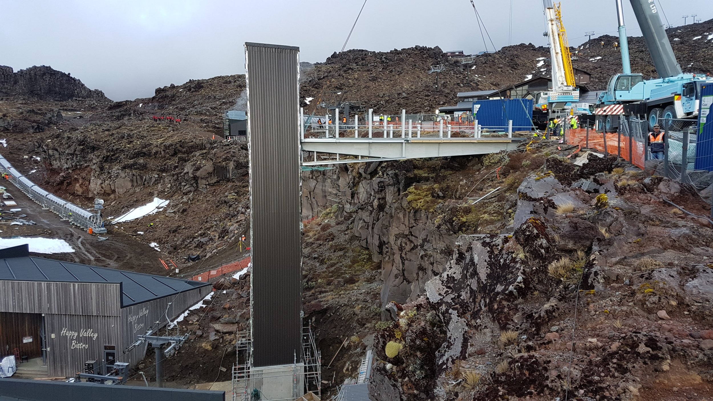 Construction site on a mountain, with cranes, construction workers, a bridge, and a building labeled 'Happy Valley Bistro'.