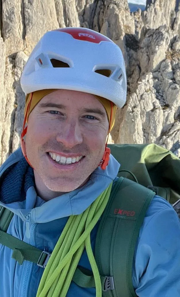 Ein Mann beim Klettern in den Bergen, trägt einen Helm und einen Rucksack.