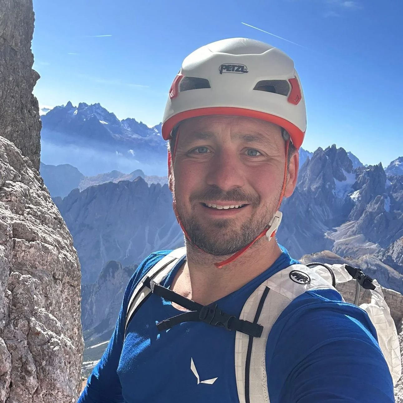 Mann mit Kletterhelm und Rucksack vor Bergkulisse in den Alpen.