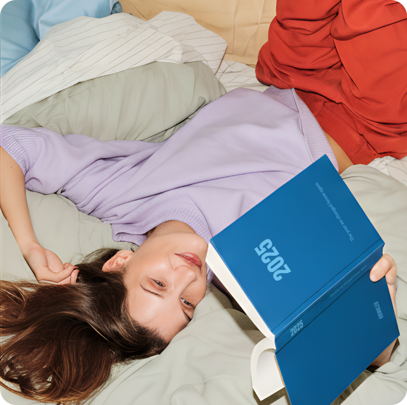 Woman lying on bed laughing while holding Krinkled blue hardcover family book from 2023