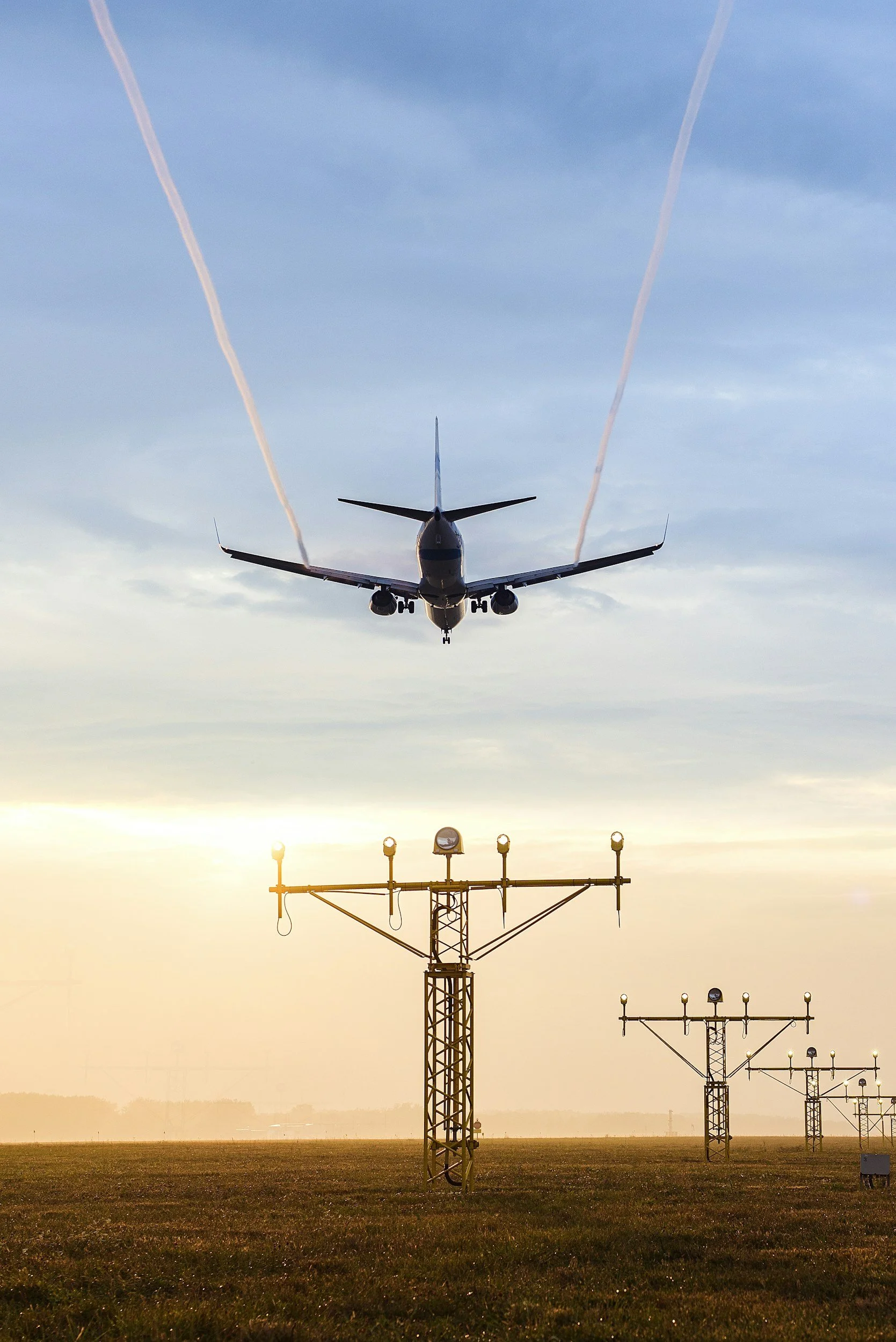 Airplane flying just above about to land on the runway at sunset, with airport lights on the control tower visible below.