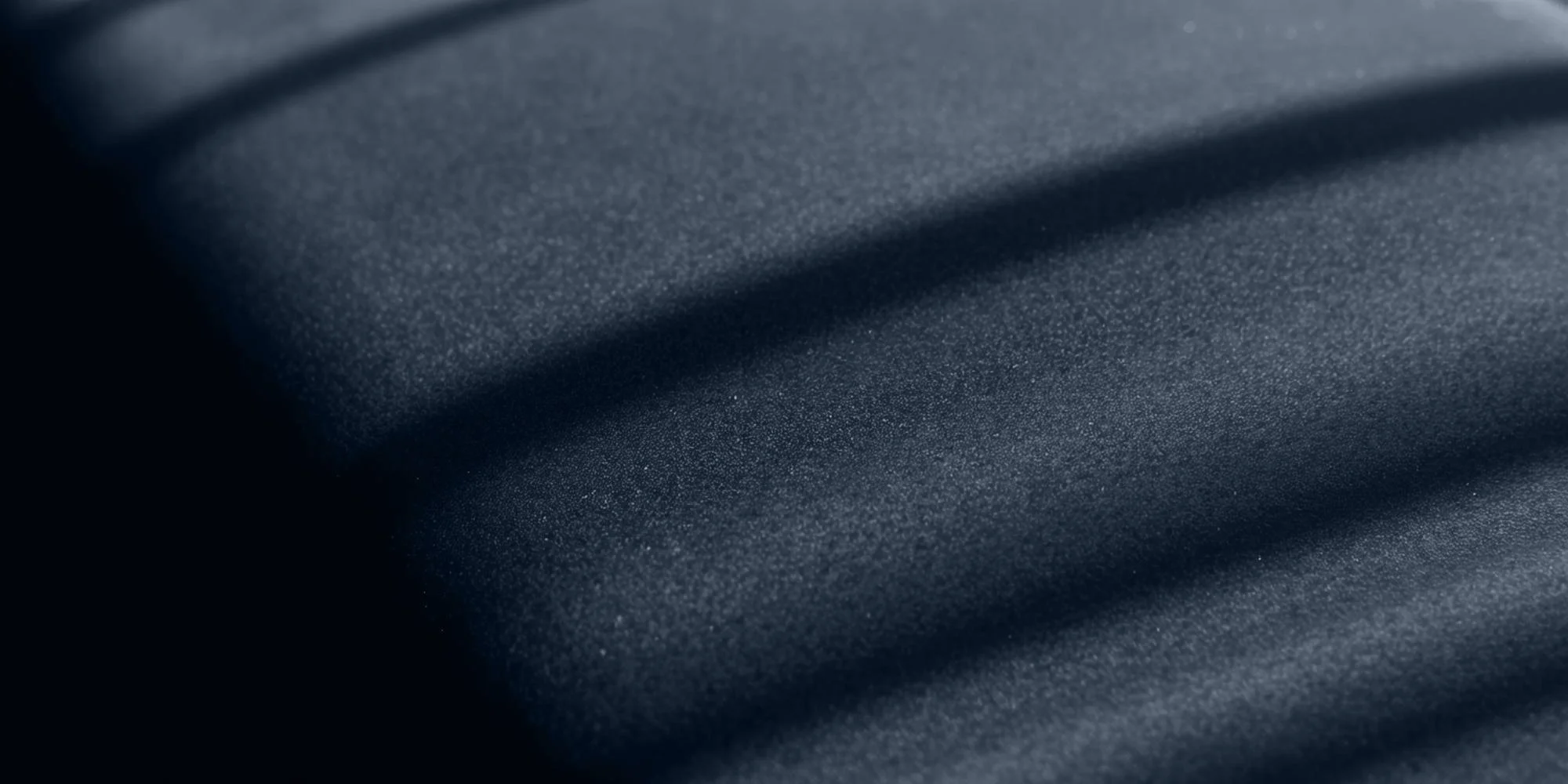 Close-up of a dark textured fabric with shadows and light reflecting off its surface.