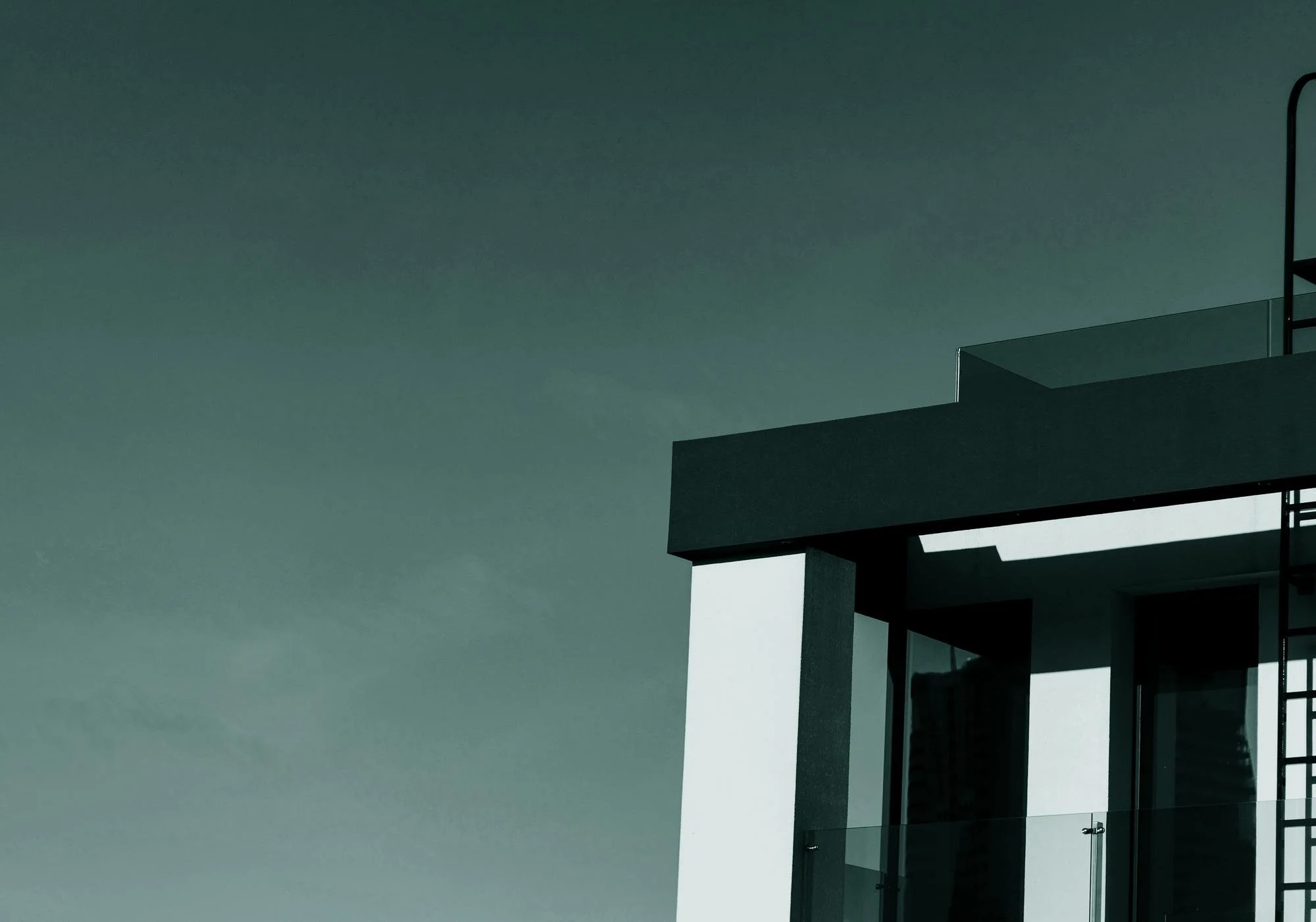 Close-up of a modern building with glass balcony and dark overhang against a gray sky.