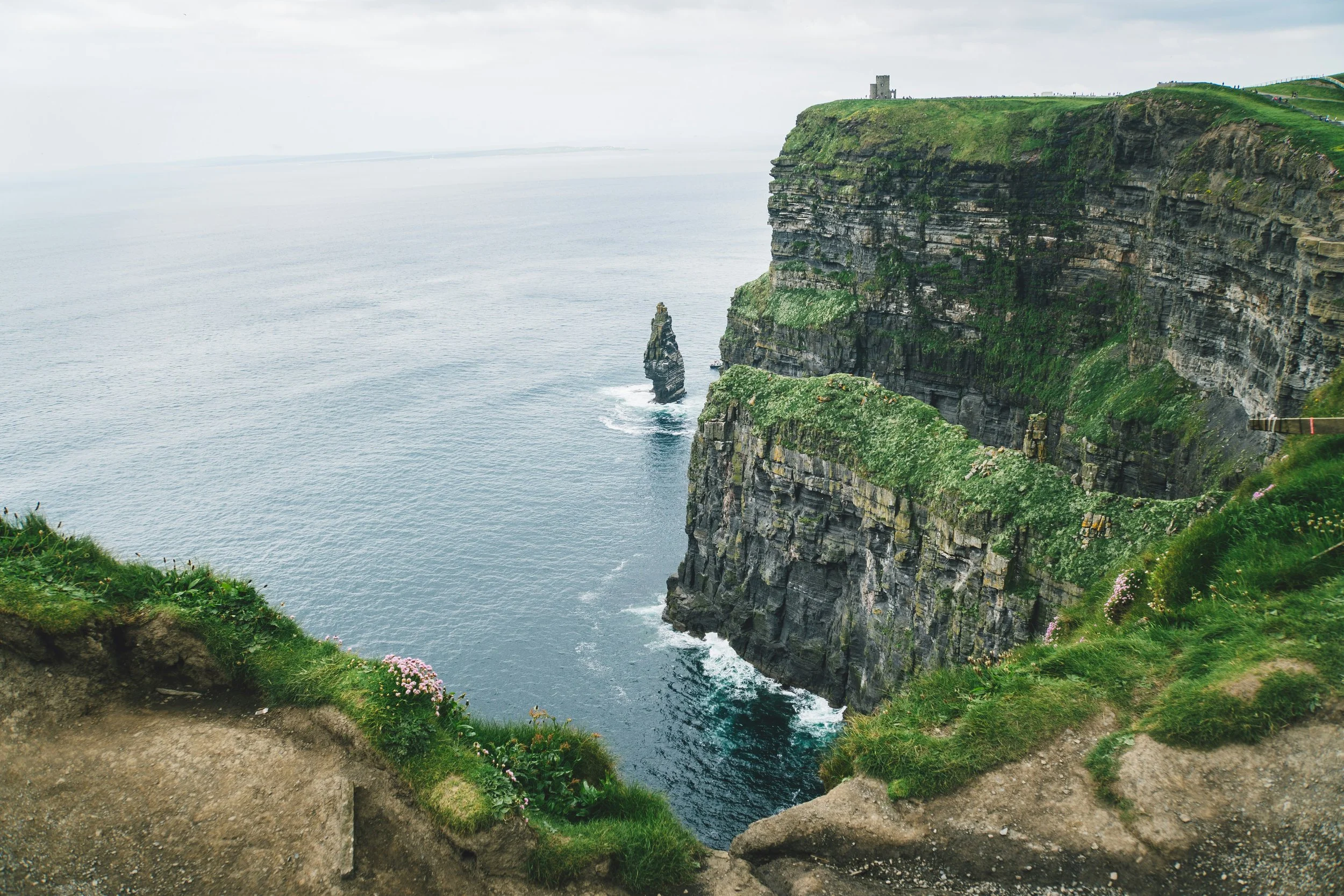 Cliffs overlooking the Atlantic Ocean, with a small castle on top and a rocky sea stack in the water.