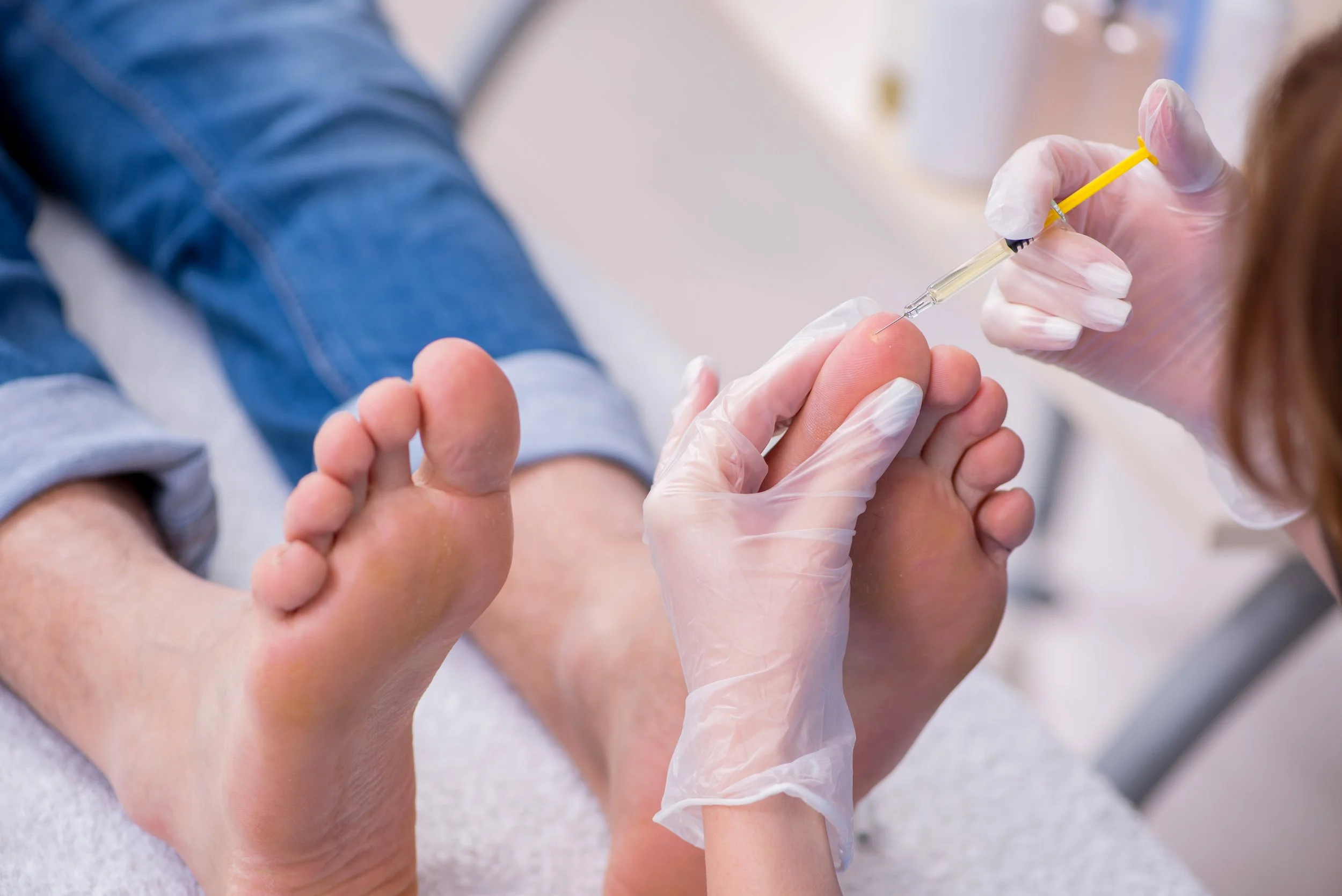 A healthcare worker administering a foot injection to a patient in a clinical setting.