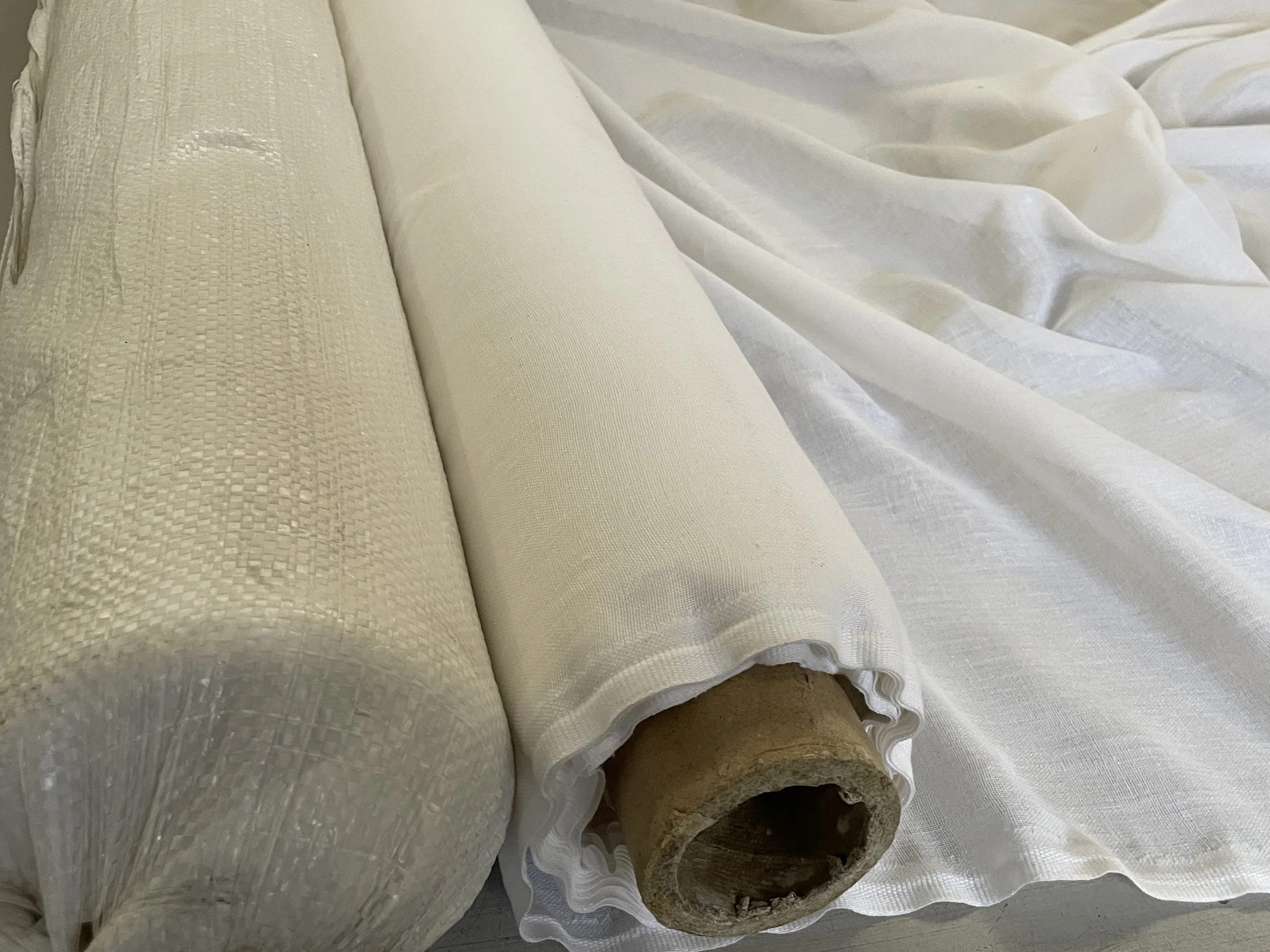 Three rolls of cream-colored fabric and a wooden rod on a white surface, with one fabric partially unrolled.