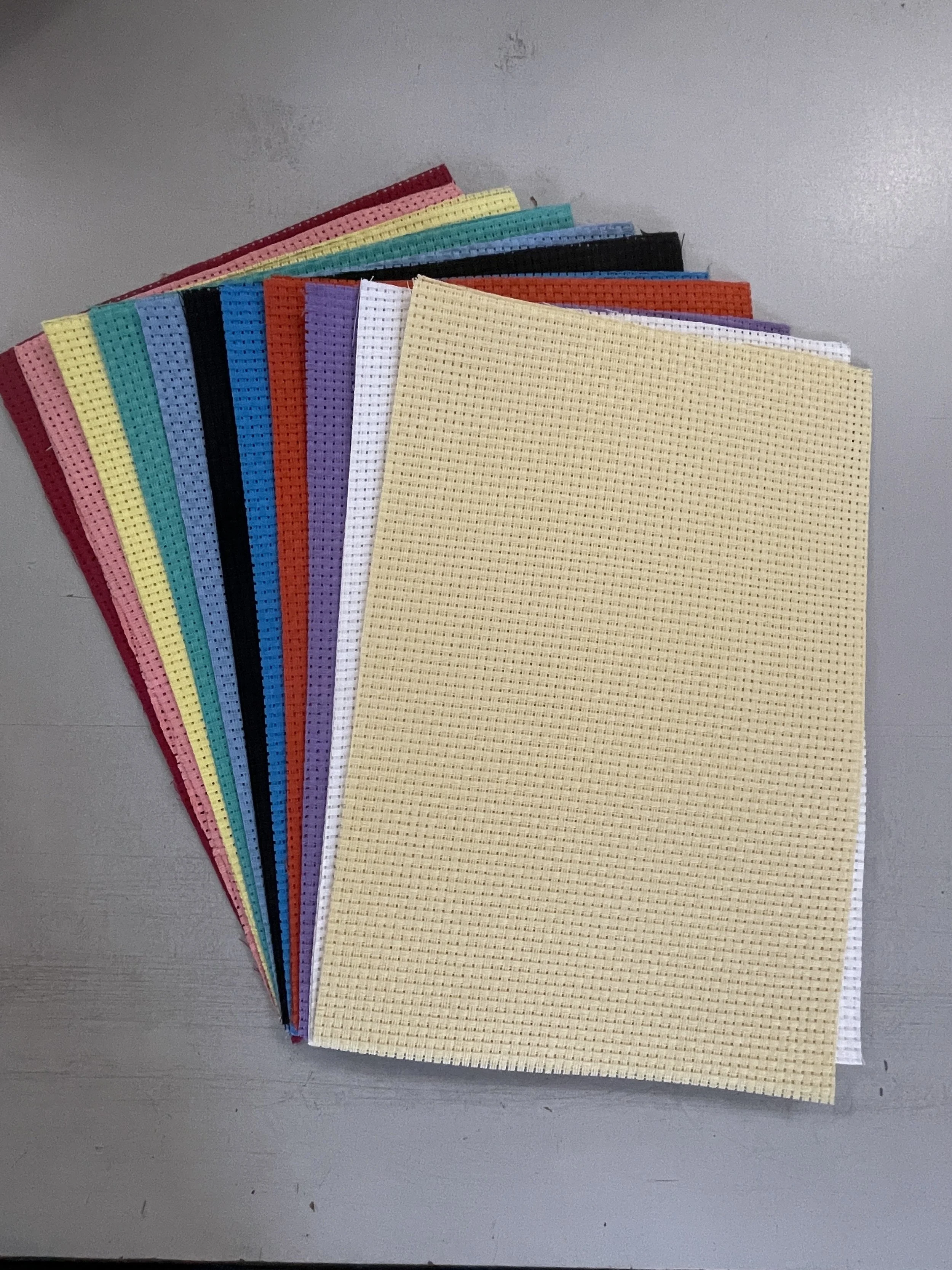 Assorted colorful plastic canvas sheets arranged in a fan shape on a gray surface.