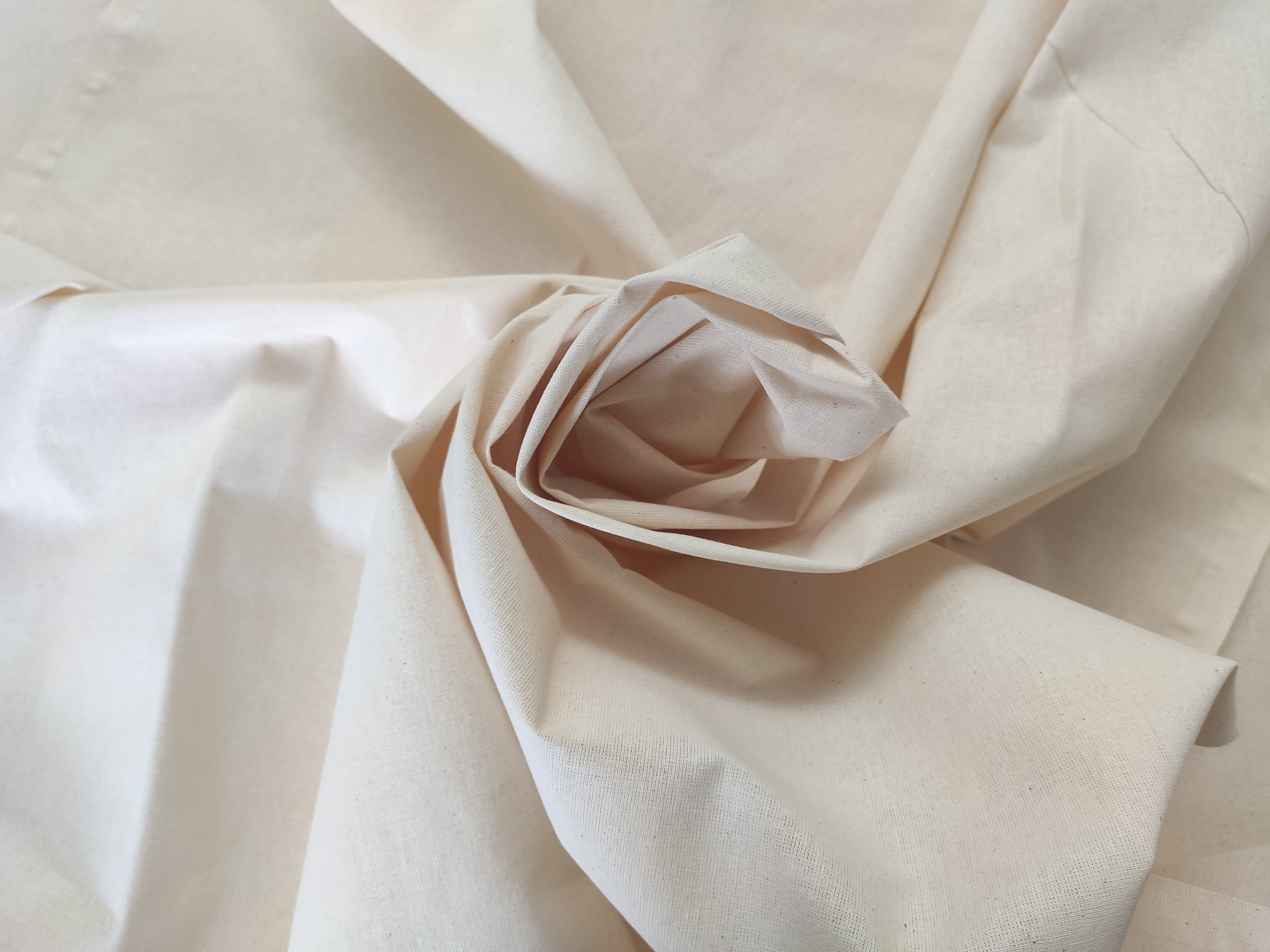 Close-up of a cream-colored fabric folded and arranged with a rolled section at the center.