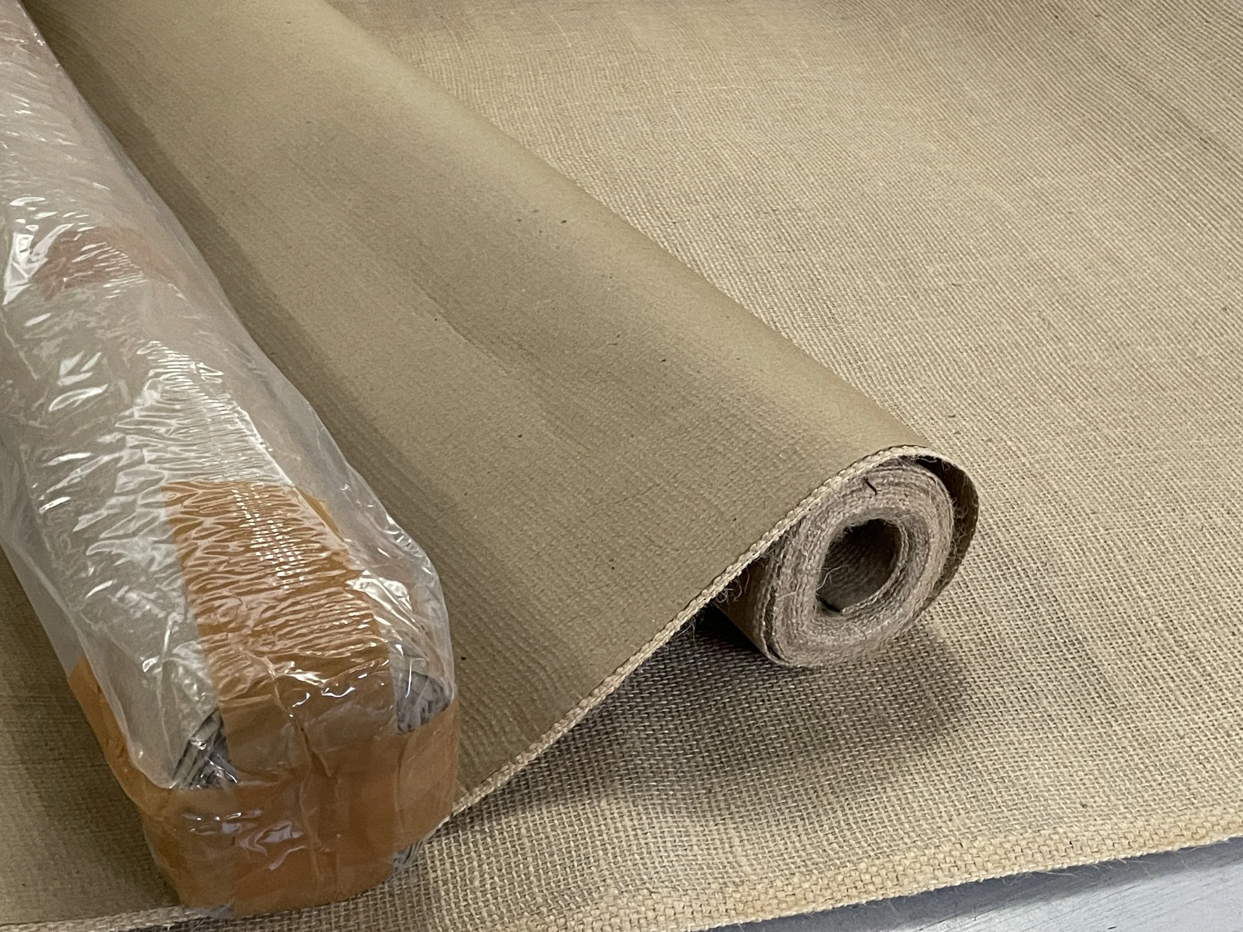 A roll of beige fabric or material partially unrolled on a matching surface, with a plastic bag containing smaller items nearby.