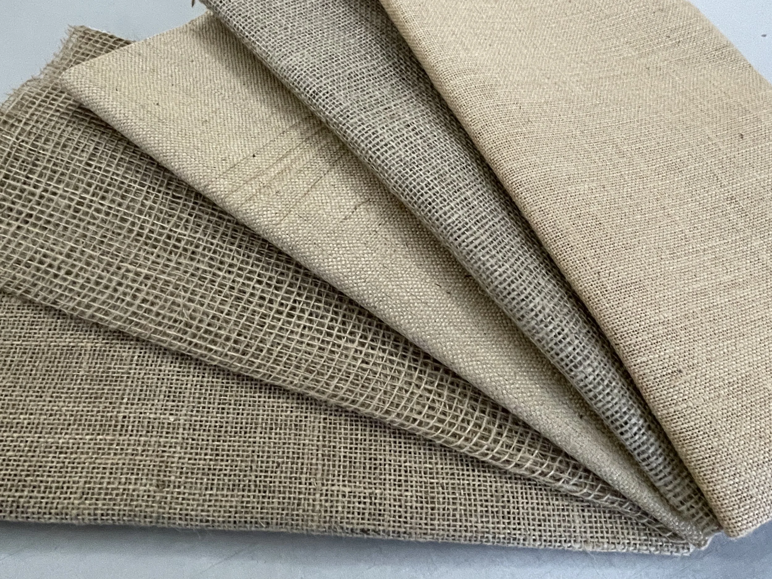 A stack of six beige and tan woven fabric swatches, stacked and folded in layers.