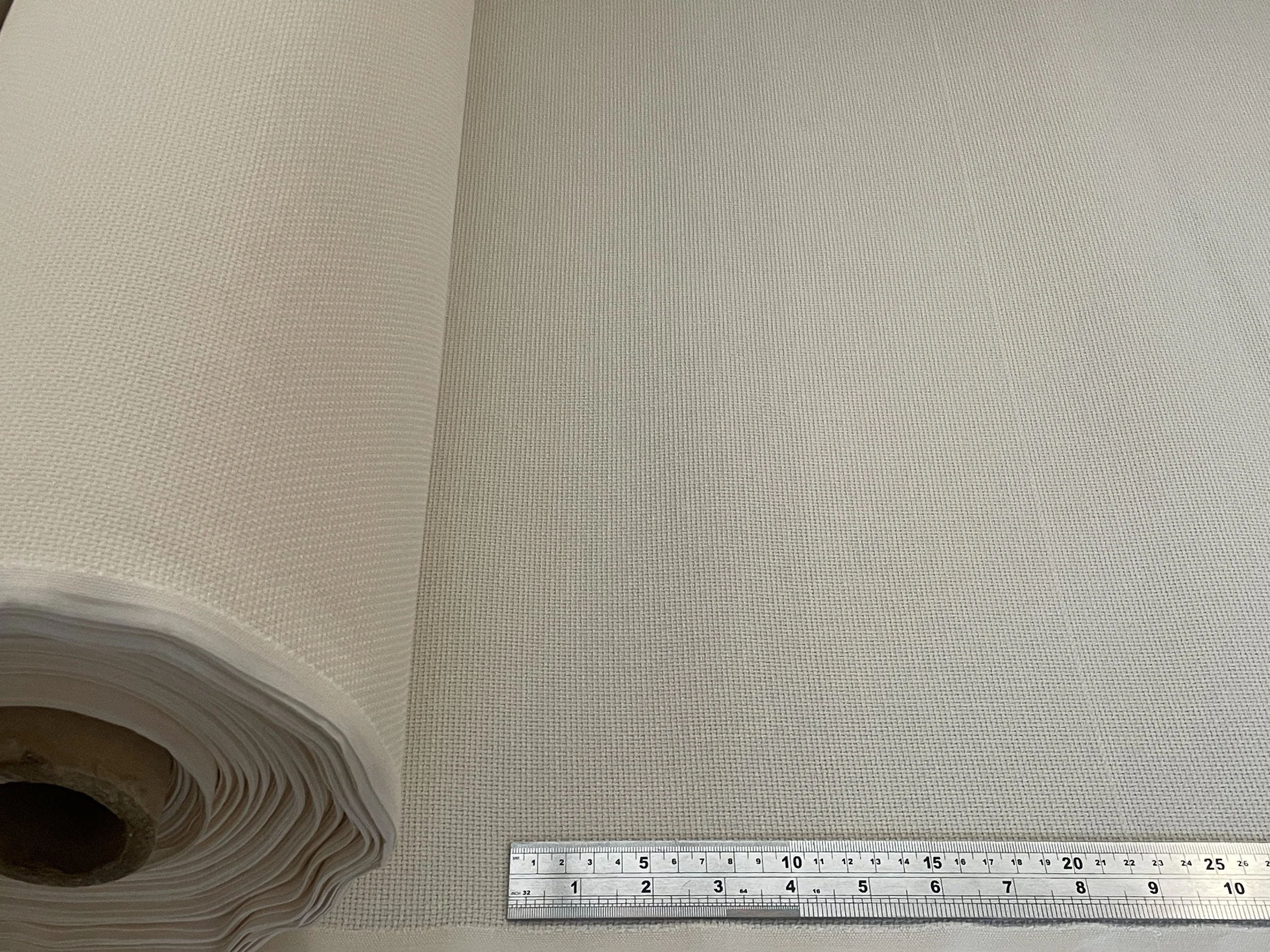 Close-up of a large roll of textured fabric or wallpaper on a table with a ruler showing measurement in inches.