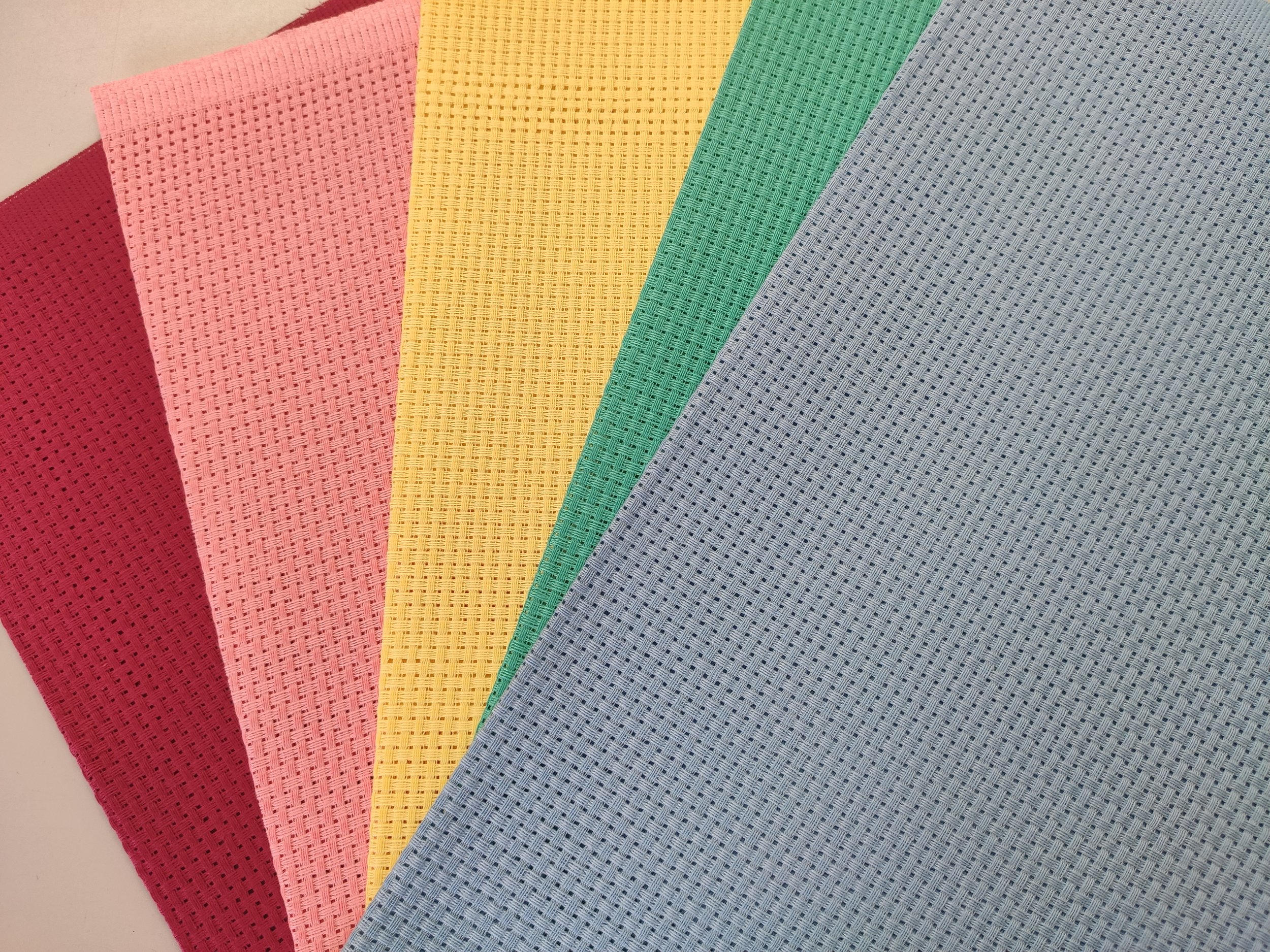 Six pieces of textured fabric in red, pink, yellow, green, light blue, and dark blue, partially overlapping each other.