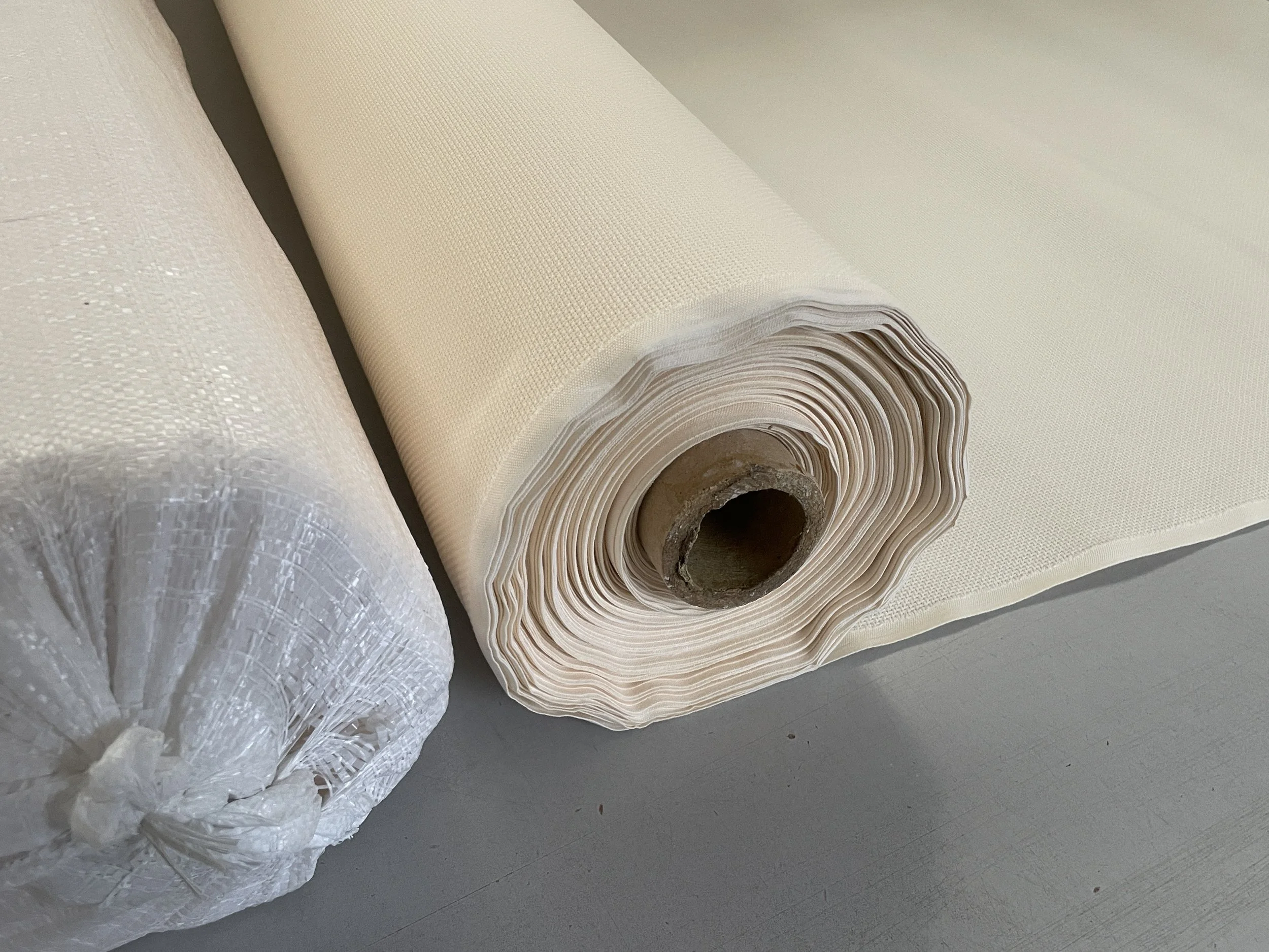 Two rolls of textured fabric or liner on a gray surface, one unwrapped and the other still wrapped in plastic.