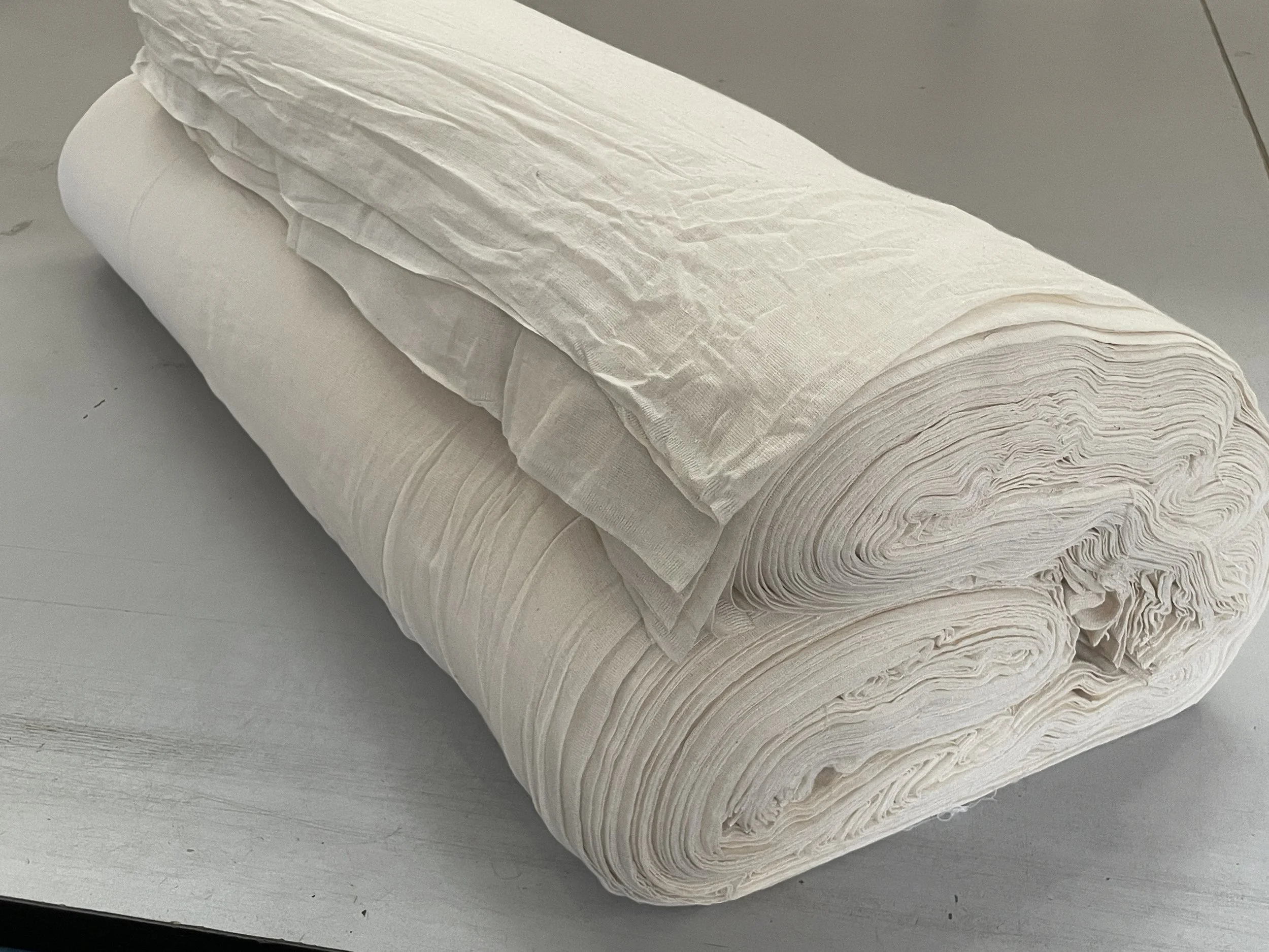 A large roll of white fabric or material with some folded layers on top, placed on a light-colored surface.