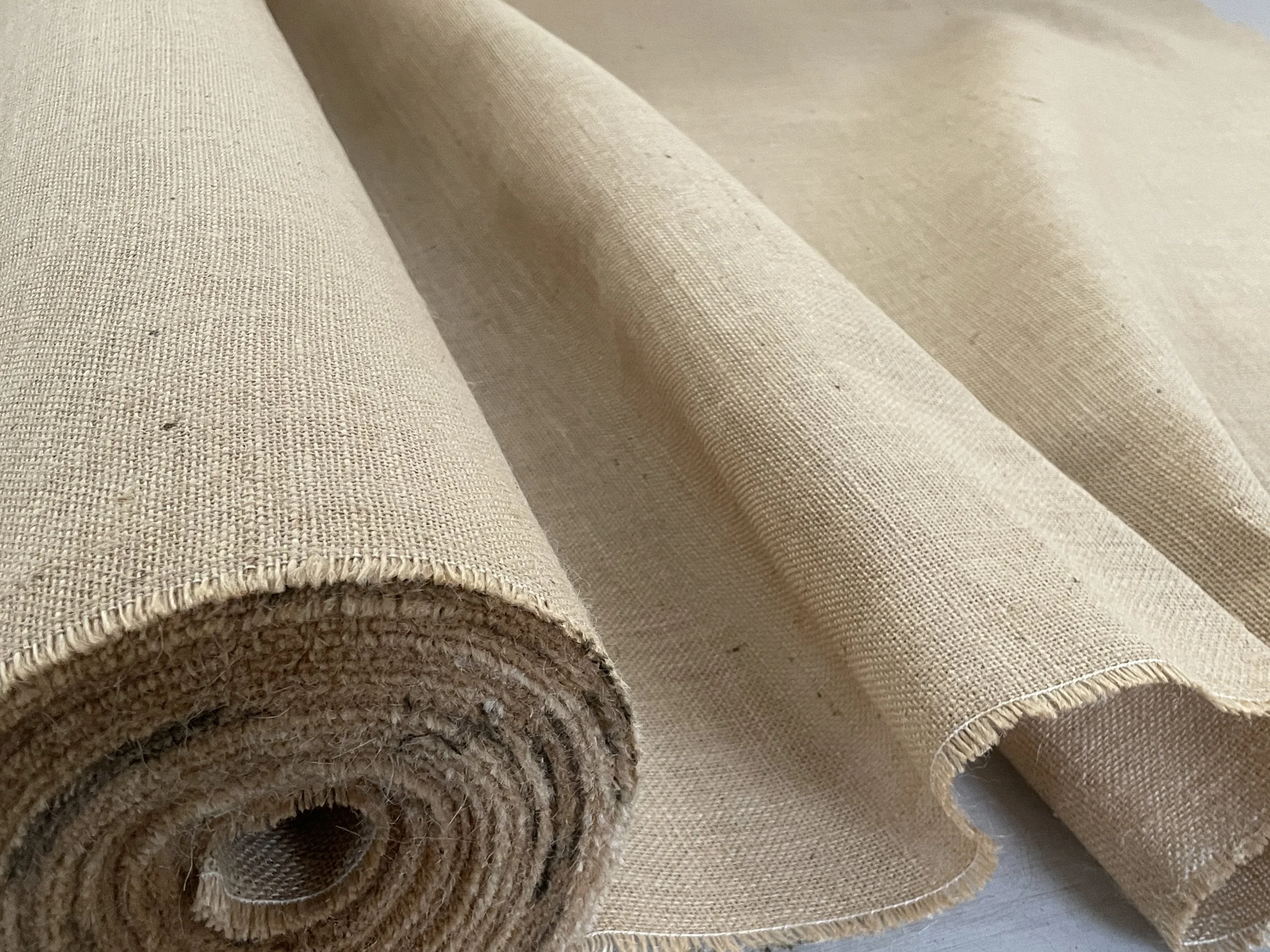 Beige woven fabric roll partially unrolled with one edge slightly curled.