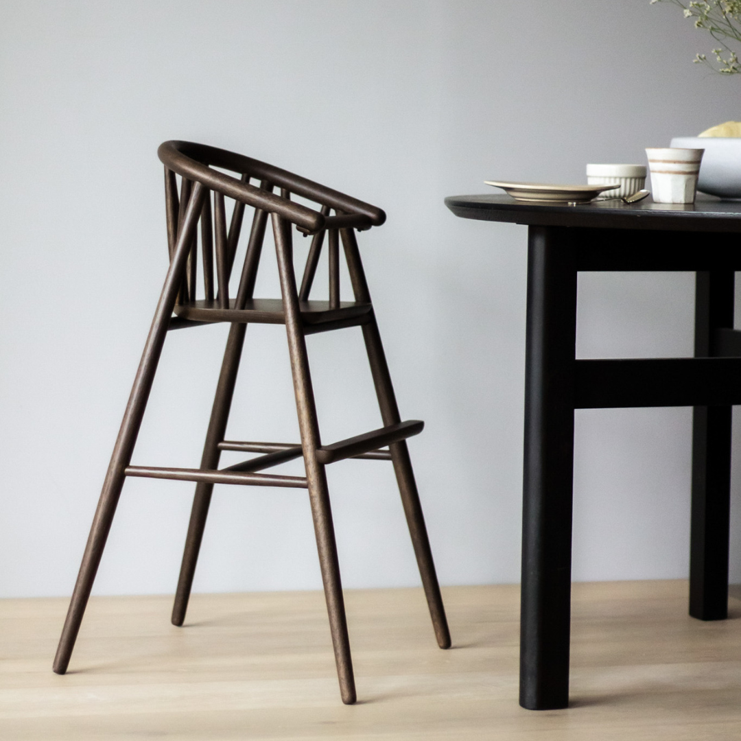 En modern spisestue med en høj træstol og et sort spisebord med tallerkener og kopper.