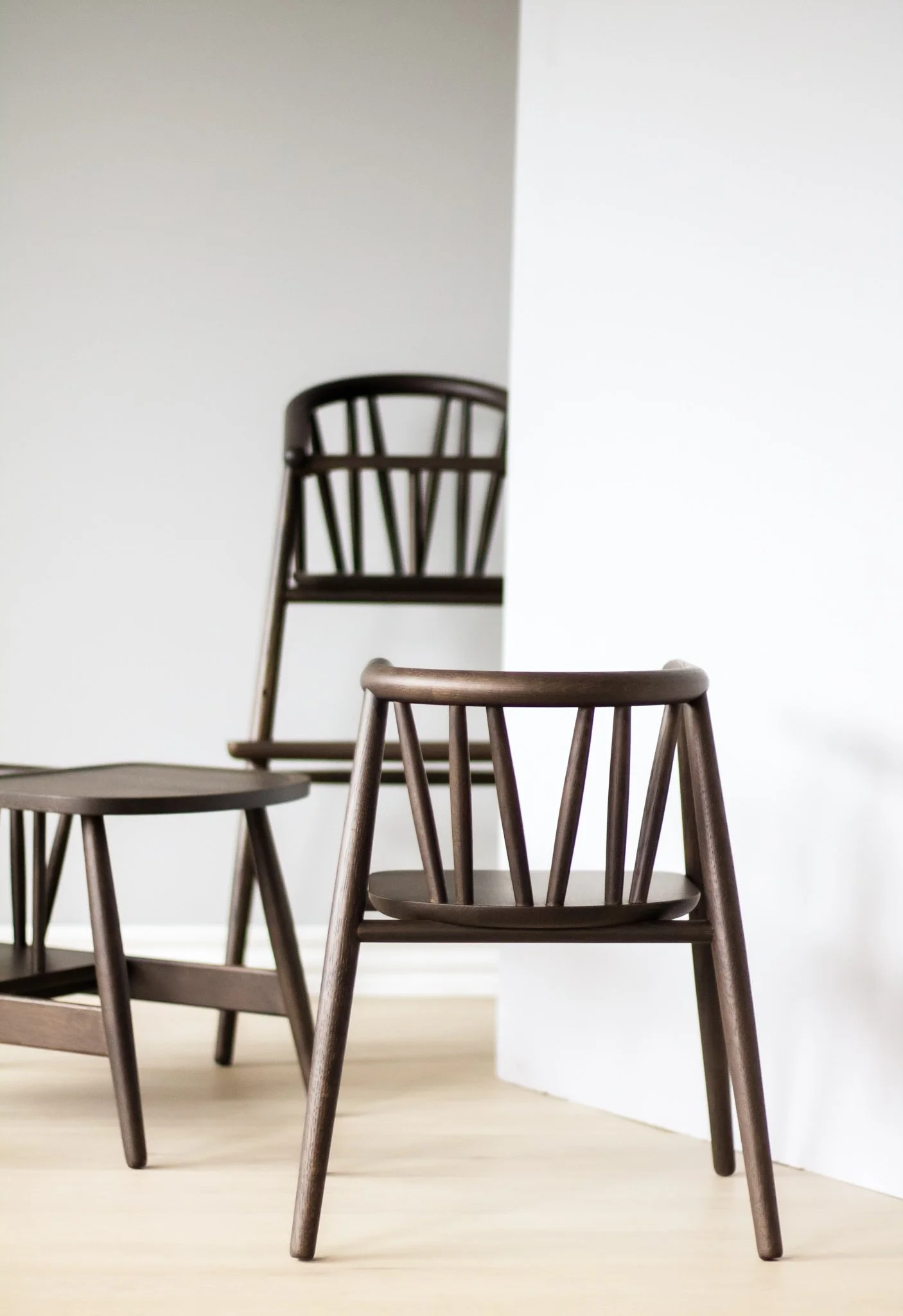 To træstole i træ, en på gulvet og en anden på en højere over fladen, med en væg og en hvid væg i baggrunden.