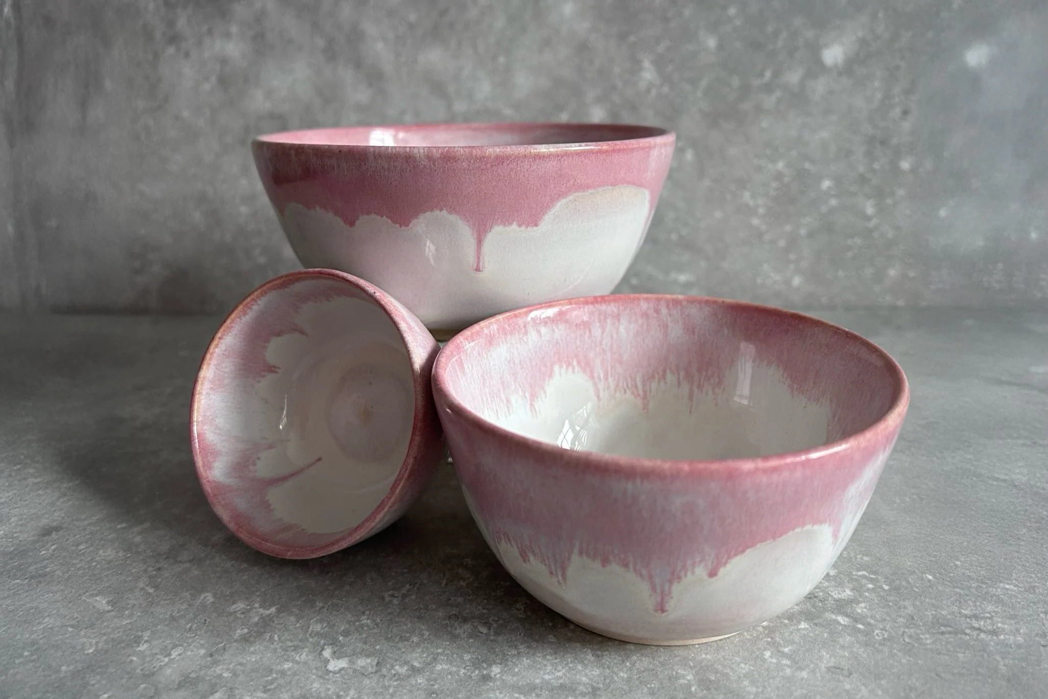 Three pink and white stacking ceramic stacking bowls on a gray surface with a gray textured background.