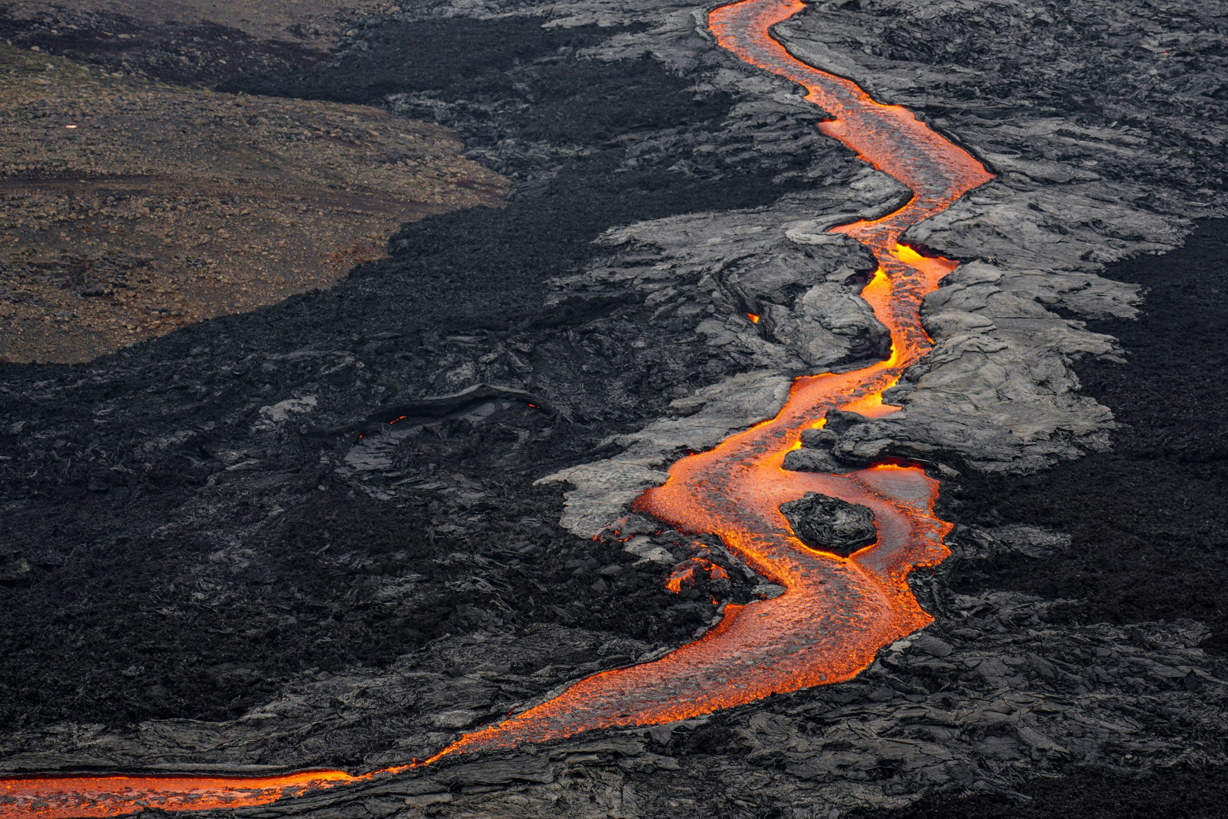 Volcanic eruption with flowing lava on dark solidified lava surface.