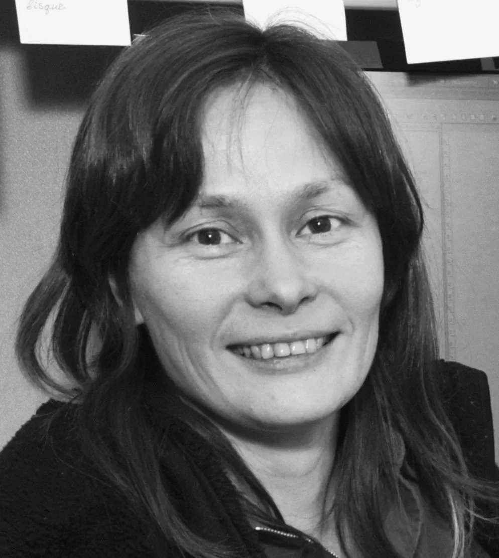 Black and white portrait of a smiling woman with shoulder-length hair in an office setting.