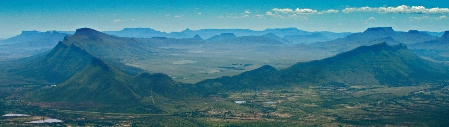 A panoramic view of a volcanic landscape with flat-topped mountains and expansive terrain under a blue sky with scattered clouds.