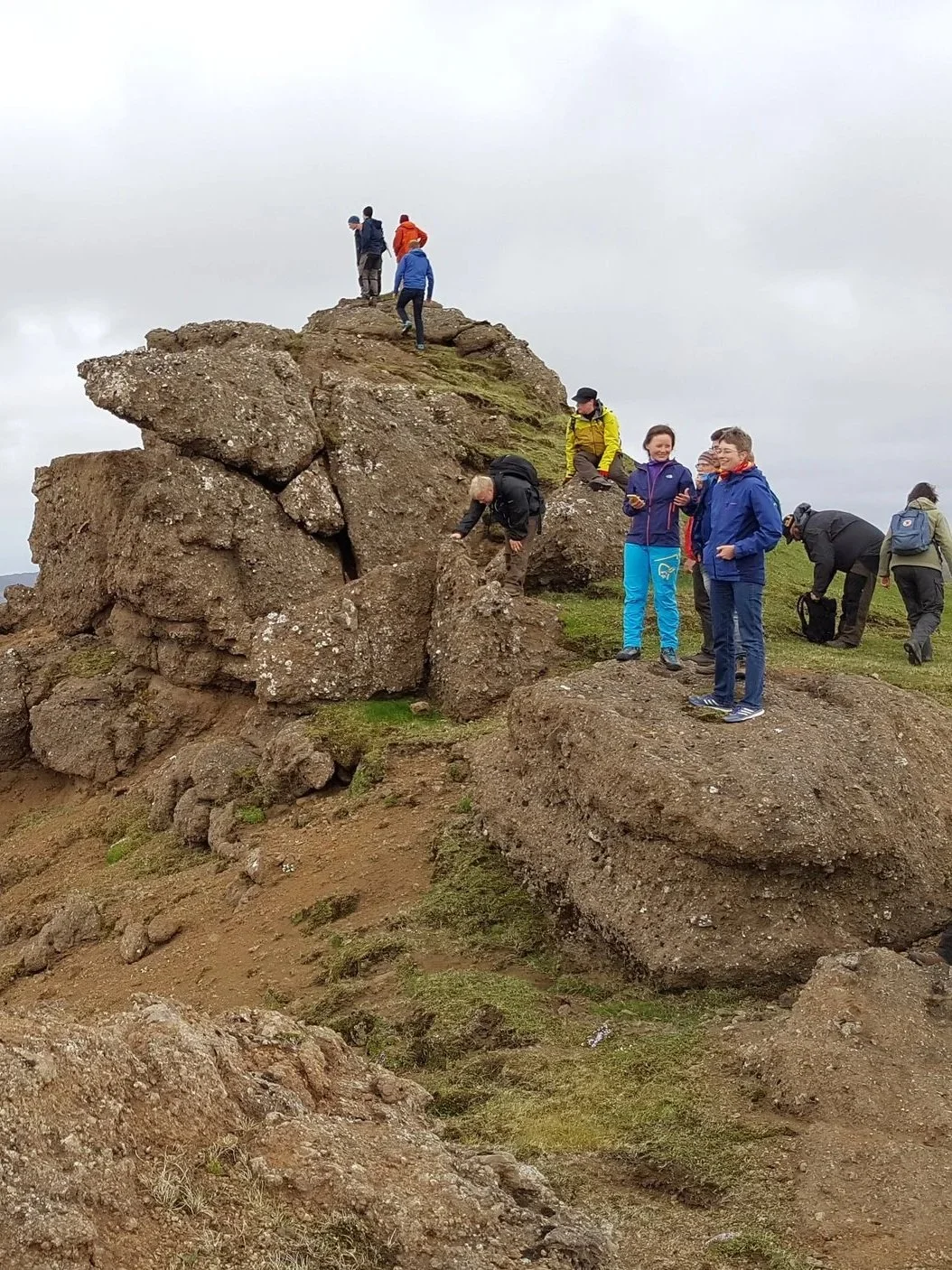Group of people hiking and resting on rocky terrain under cloudy sky.