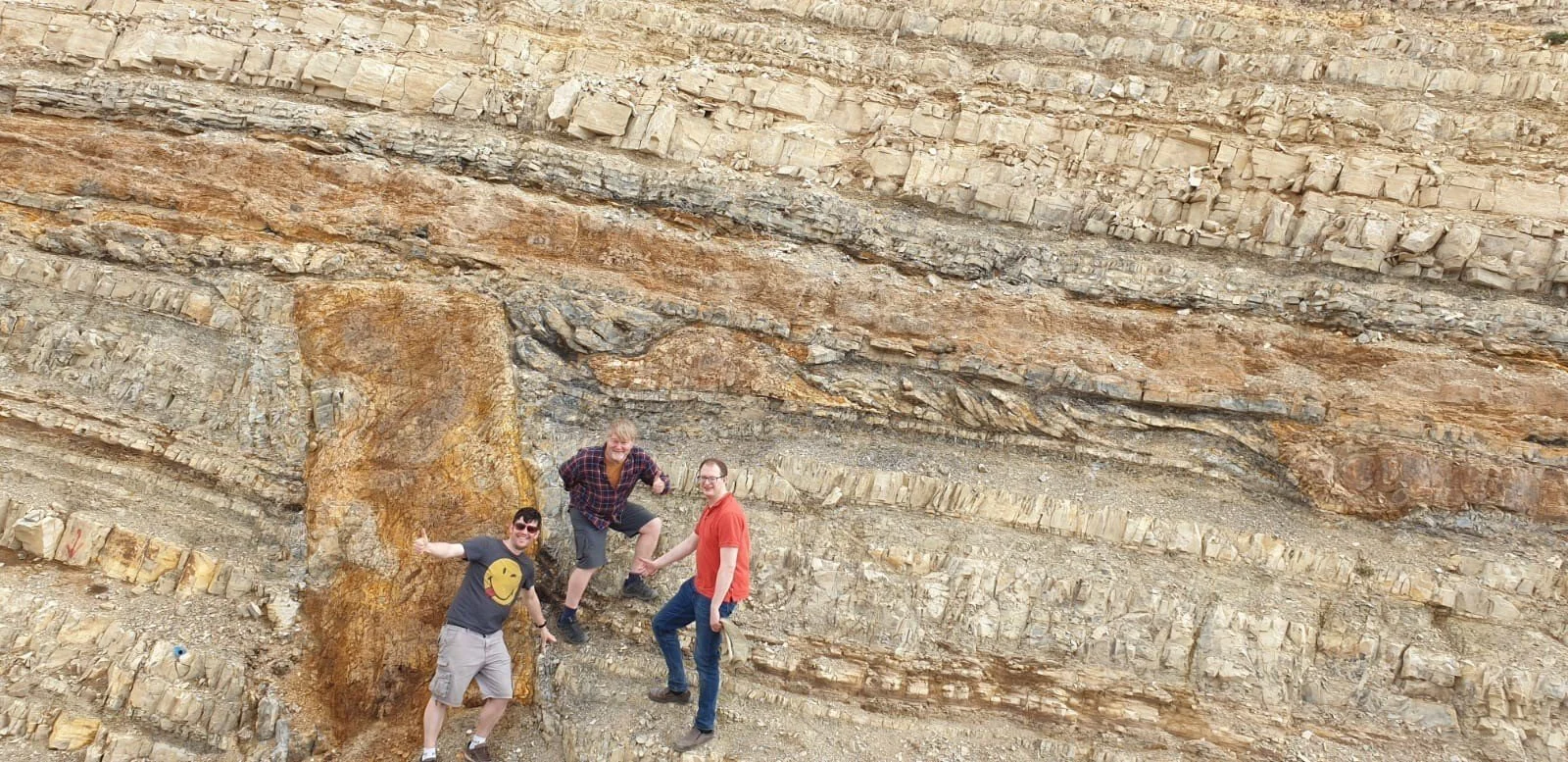 Three men are hiking on a rocky mountain slope.